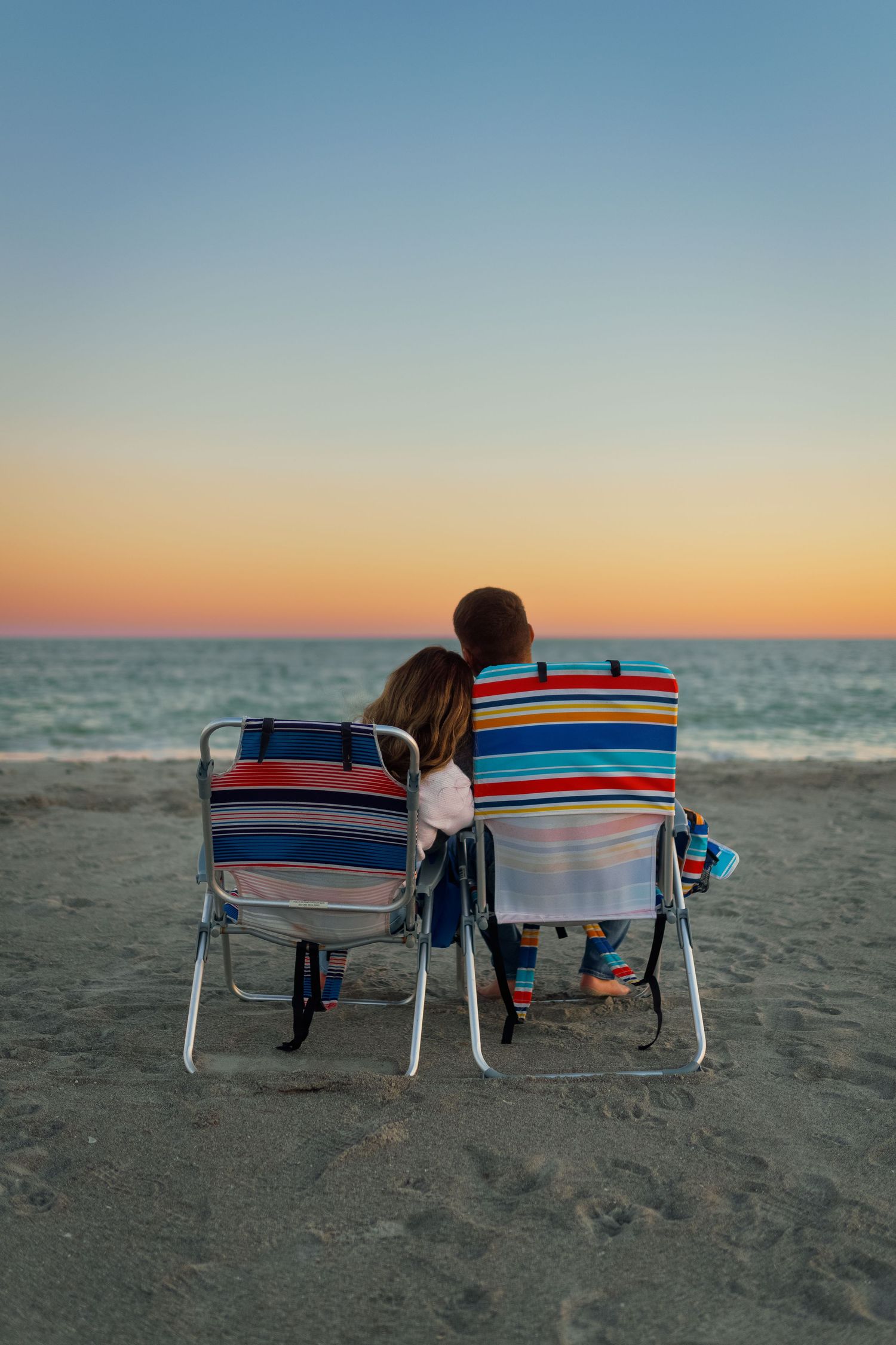 Two people relaxing in beach chairs watching the sunset over the ocean.