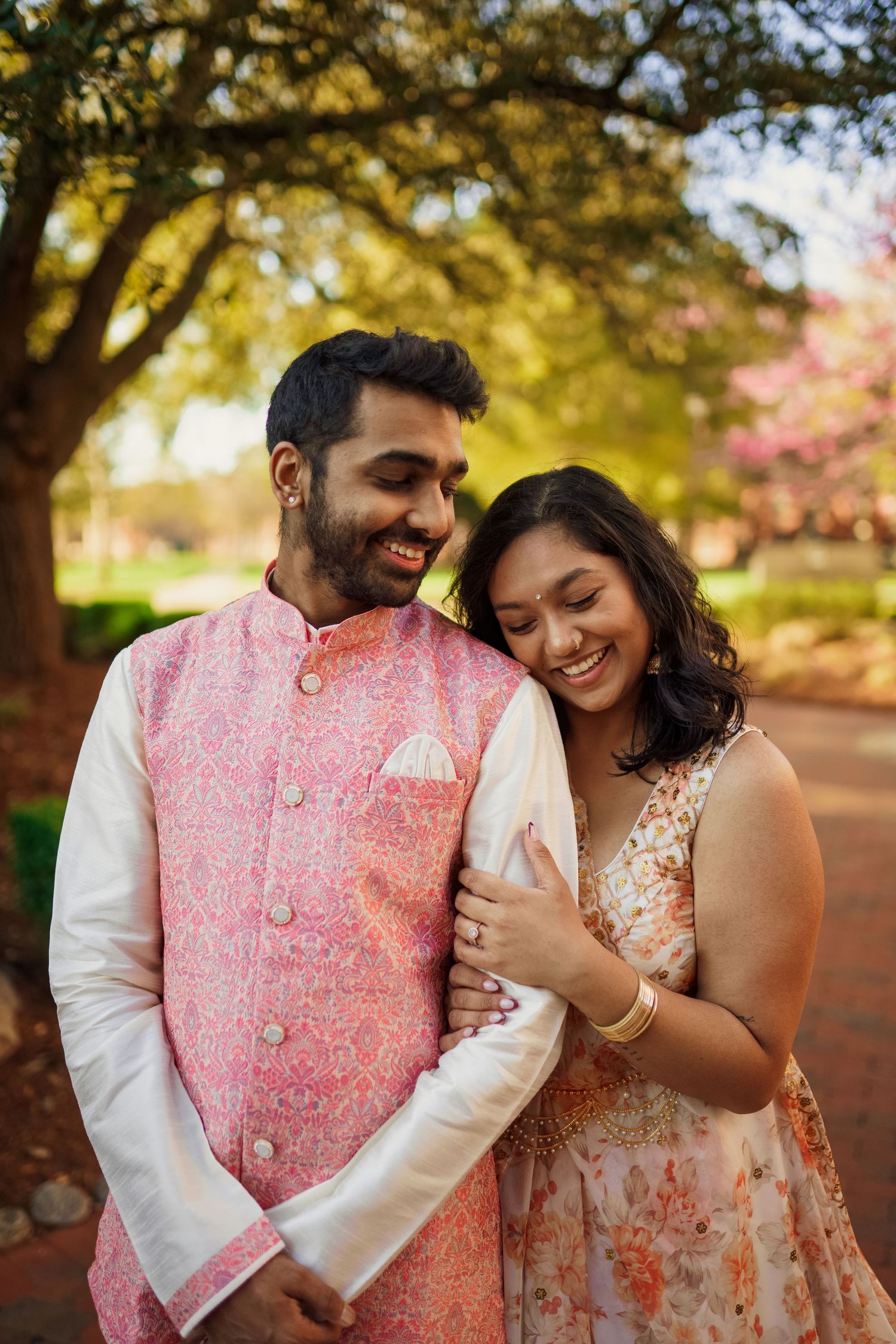 A couple in traditional Indian formal wear shares a laugh during an outdoor photoshoot.