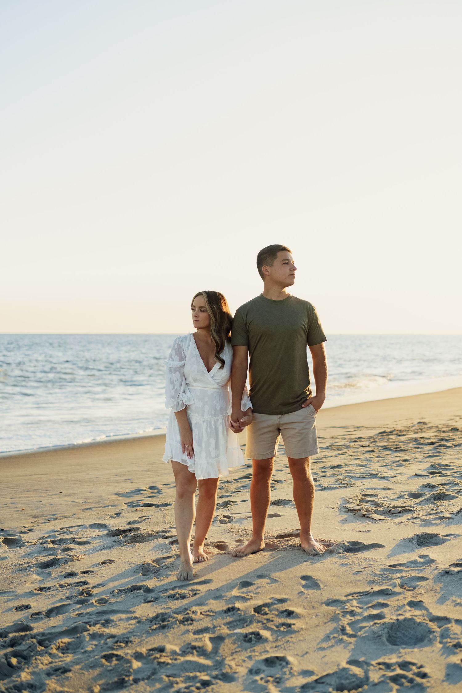 A couple in casual beach wear standing together on sandy shore.