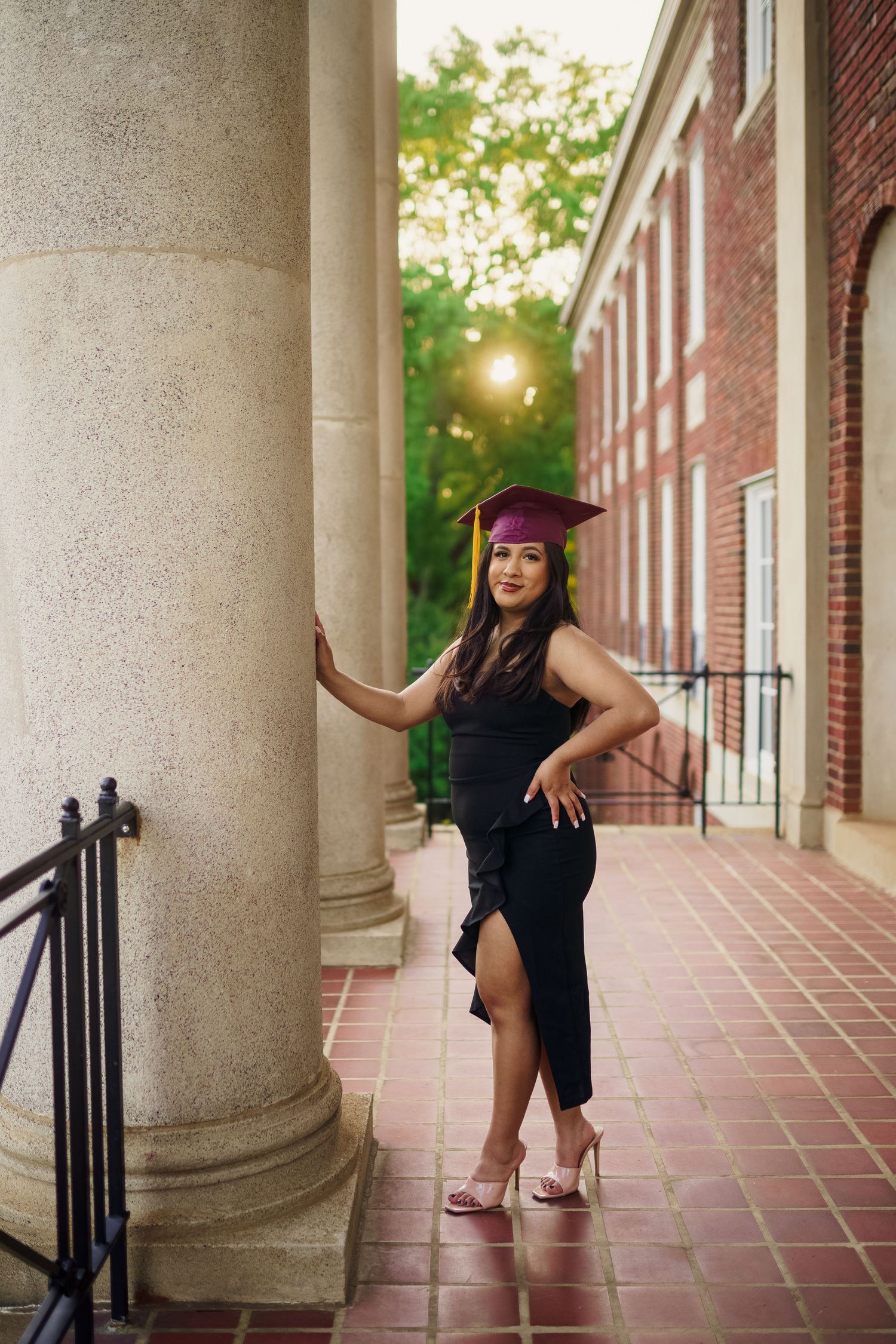 Graduate in maroon cap and gown poses elegantly against classical column architecture.