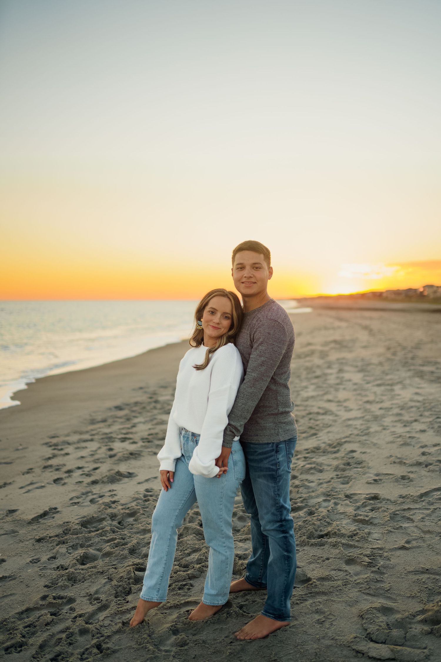 A couple standing close together on a beach at sunset.