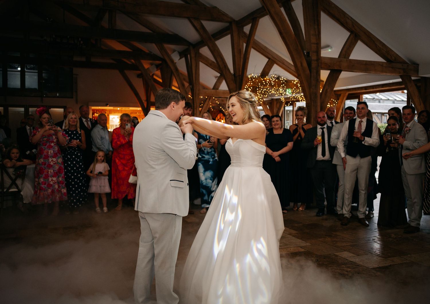 Couple sharing their first dance under rustic wooden beams at wedding reception.