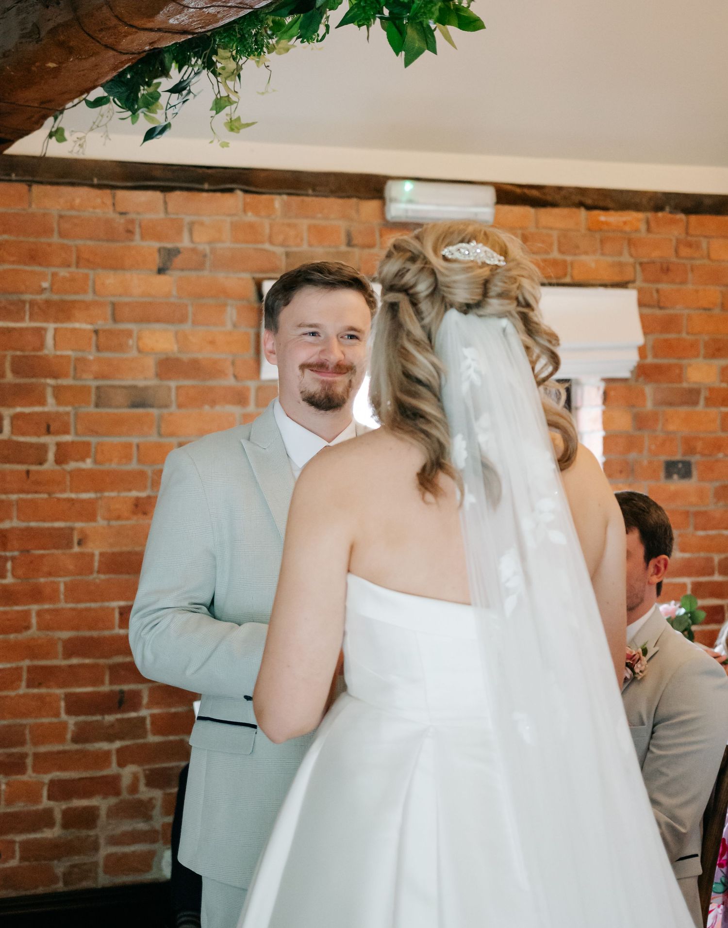 Wedding party celebrates and dances together in a rustic brick-walled venue with greenery decorations.