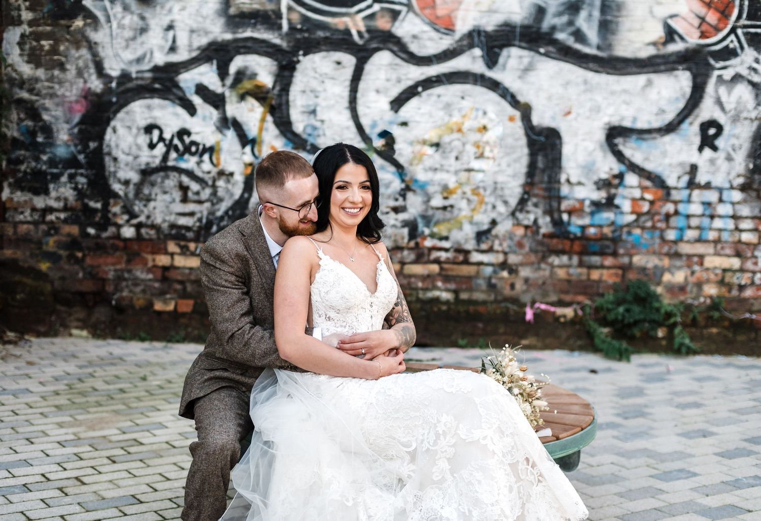 Wedding couple posing against urban graffiti wall in formal attire.