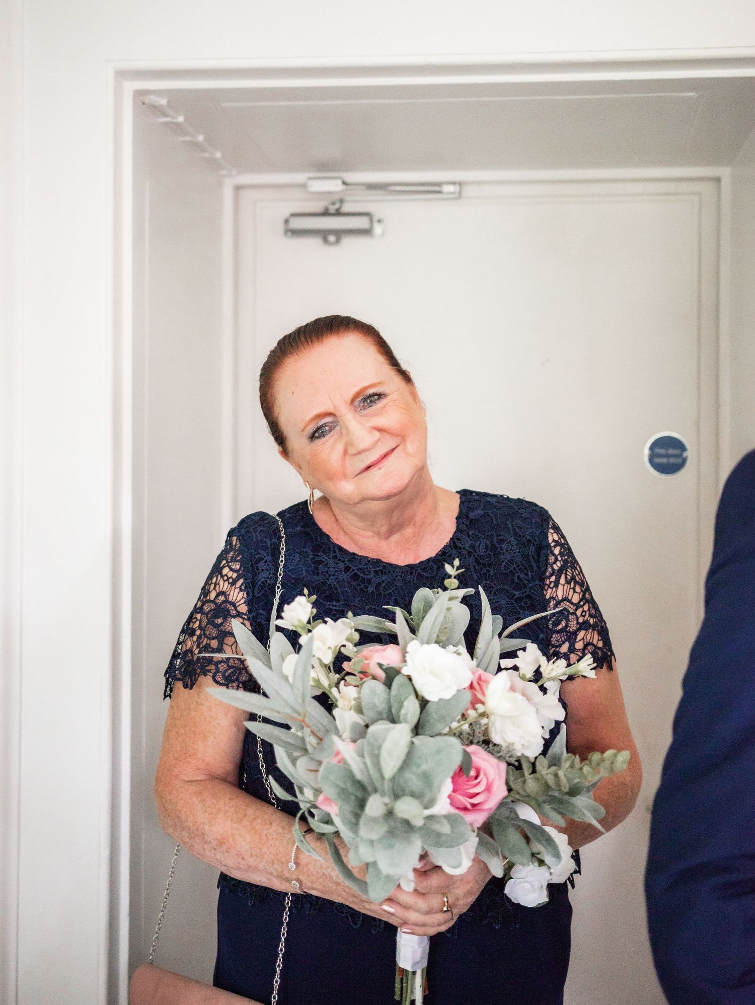 Guest in navy lace dress holds delicate pink and eucalyptus bouquet.