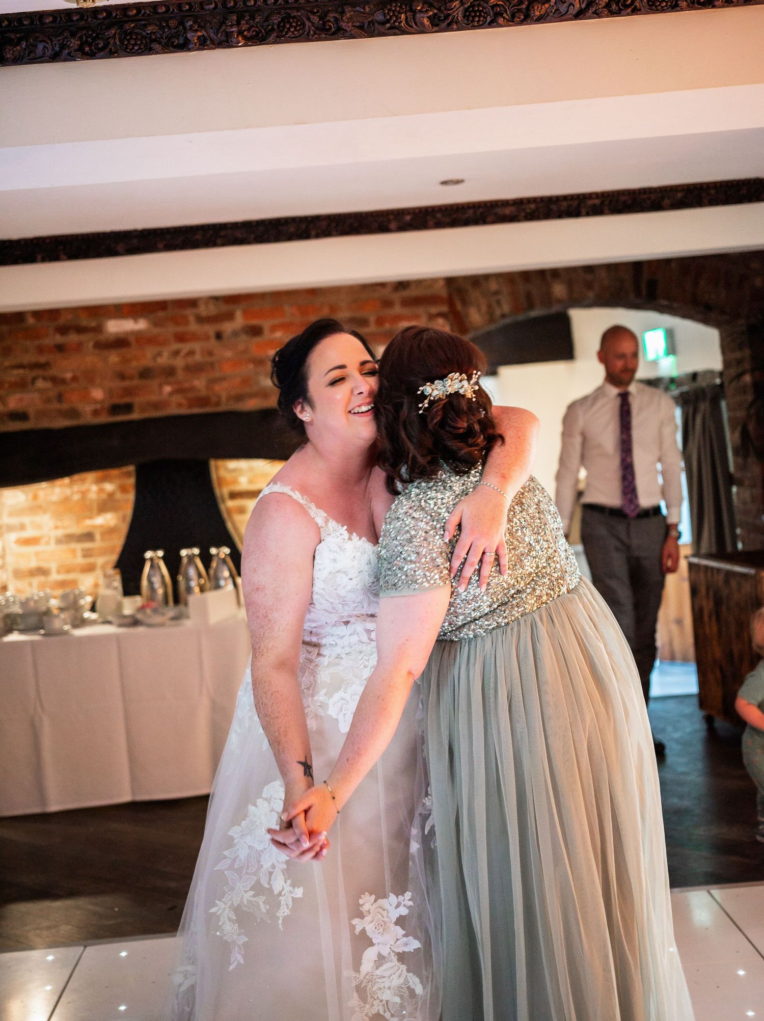 Emotional moment during wedding reception in rustic brick-walled venue.