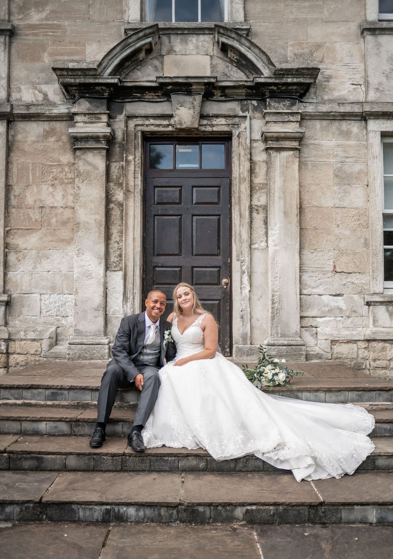 Classic wedding portrait on stone steps in front of historic doorway.