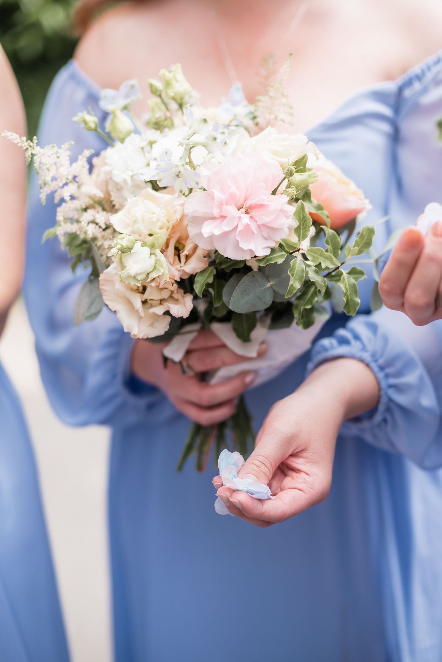 Bridesmaid in light blue dress holding delicate pink and white bouquet.
