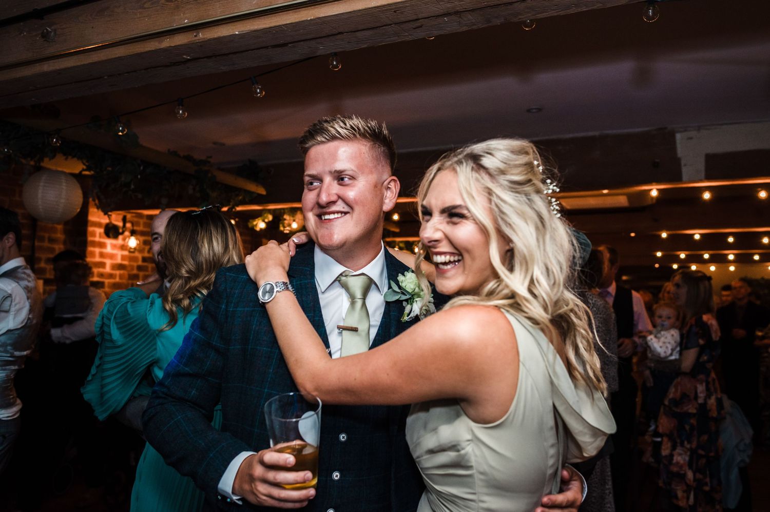 Dancing couple enjoying a celebratory moment at wedding reception with brick walls and ambient lighting.