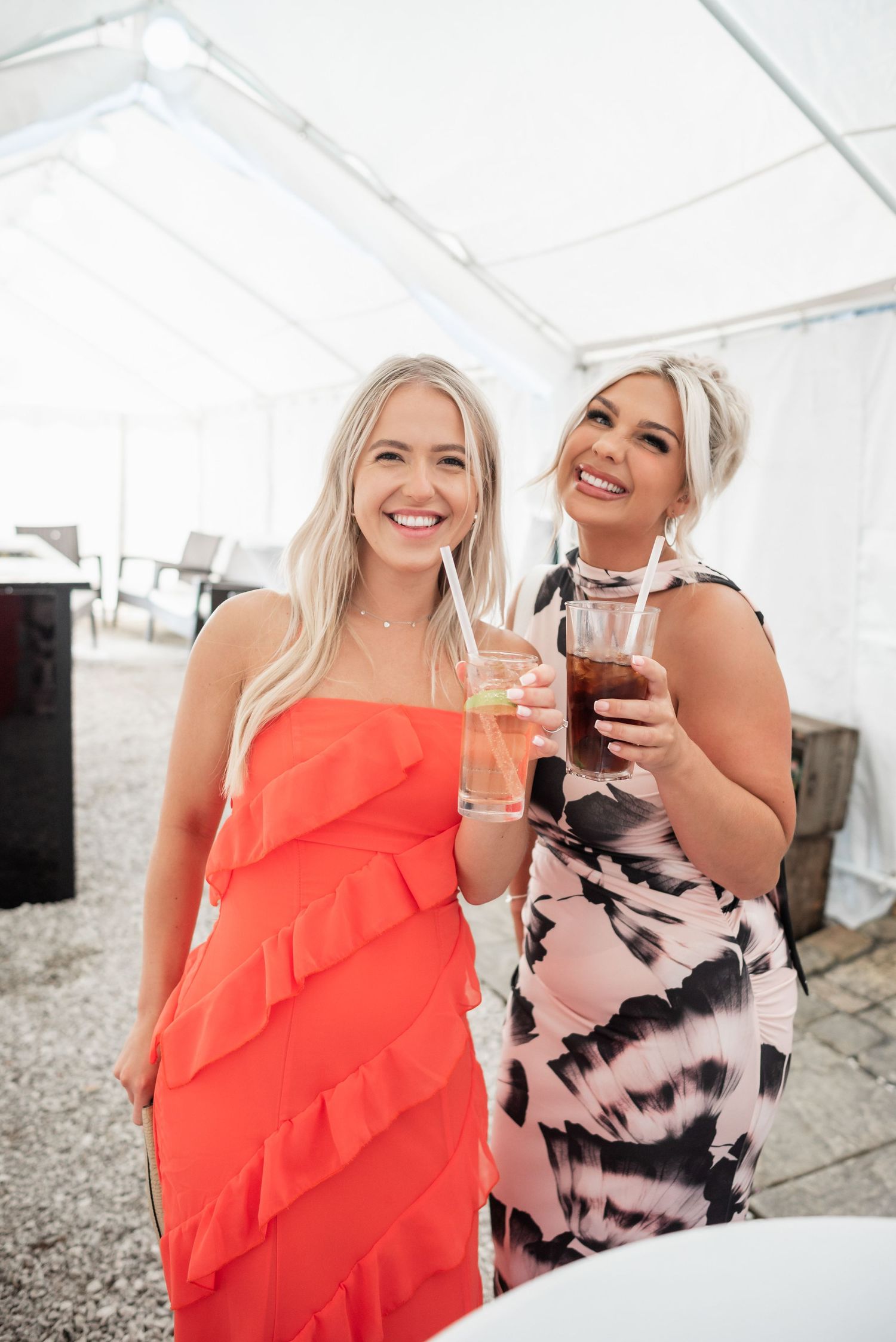 Two wedding guests in colorful dresses enjoying drinks at an outdoor reception.