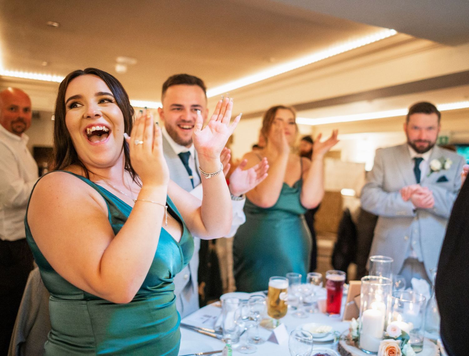 Wedding guest in emerald dress reacts with joy during reception celebration.