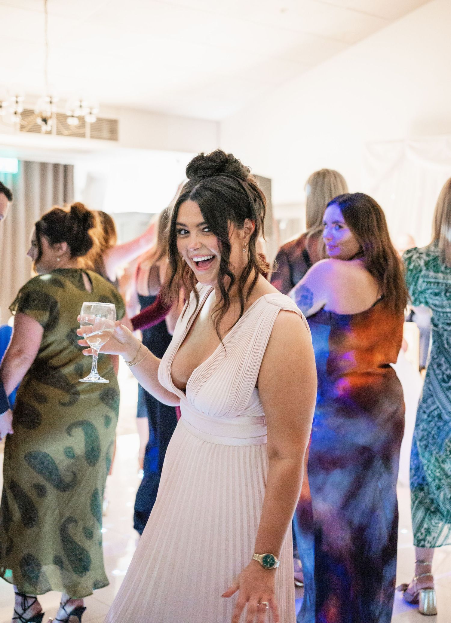 Wedding guests enjoying a celebration with colorful party lighting in a bright banquet hall.