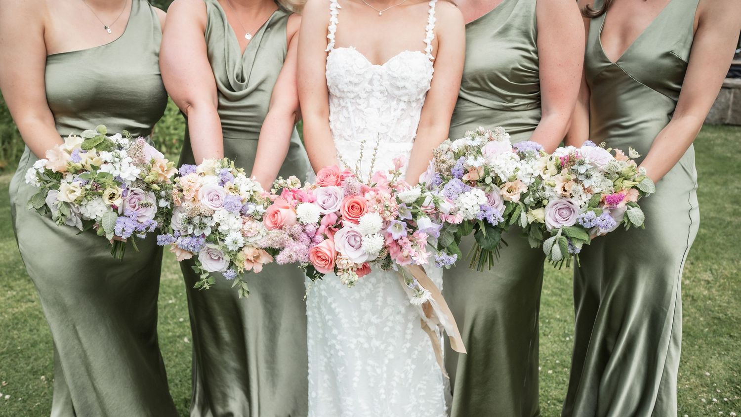 Close-up of bridesmaids holding pastel floral bouquets while wearing matching sage silk dresses.