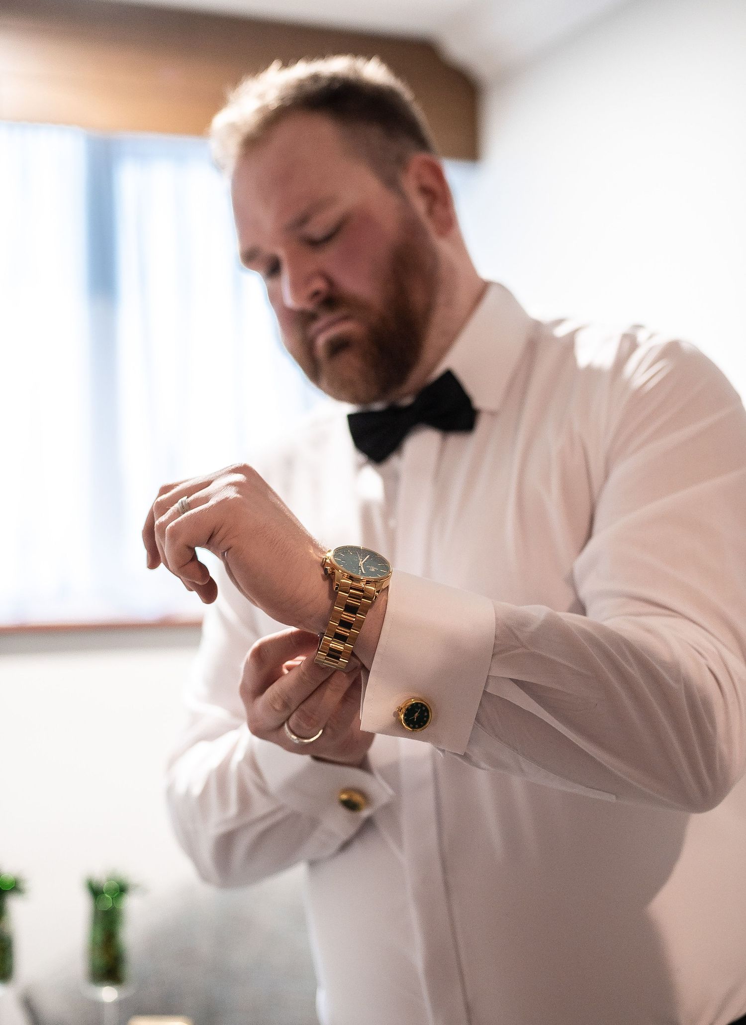 Person in formal white dress shirt and bowtie checking their gold watch while getting ready.