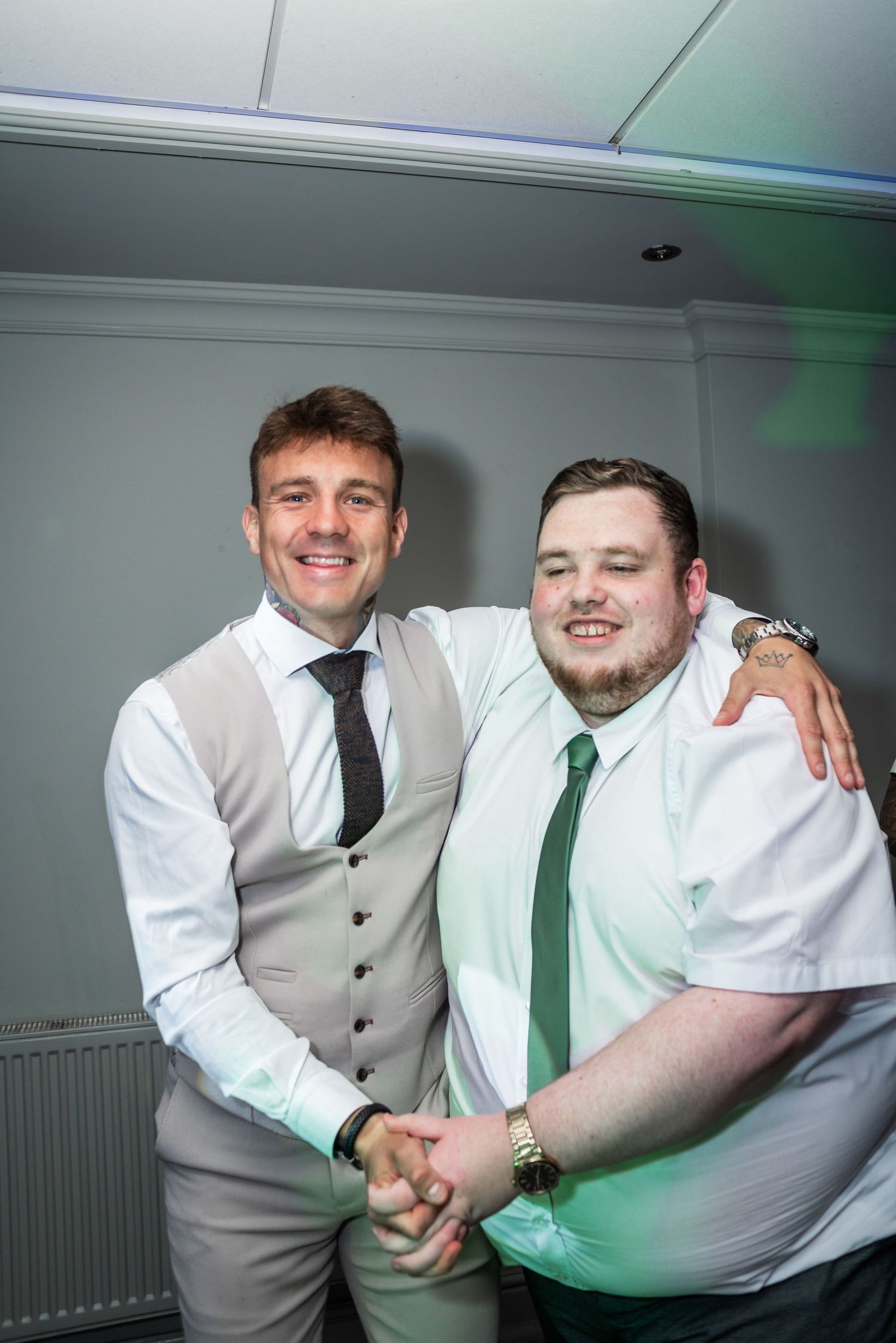 Two wedding guests in formal attire share friendly handshake at reception.