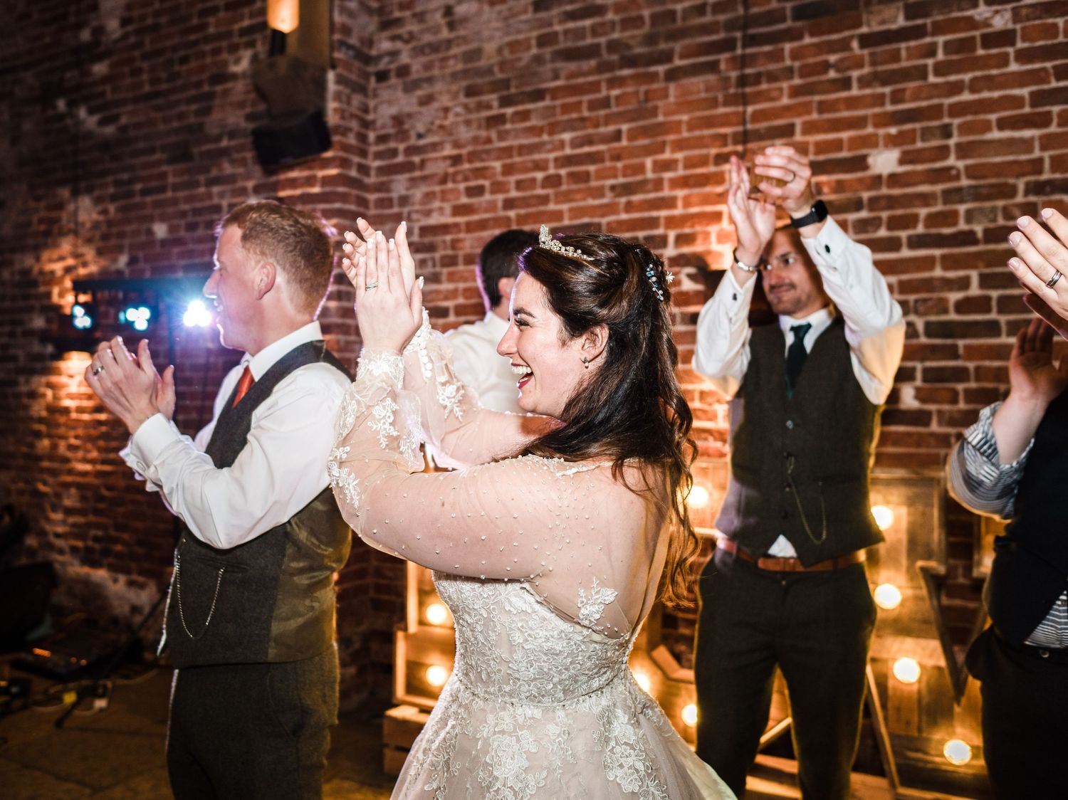 Wedding guests celebrate with raised hands and joyful expressions on the dance floor.