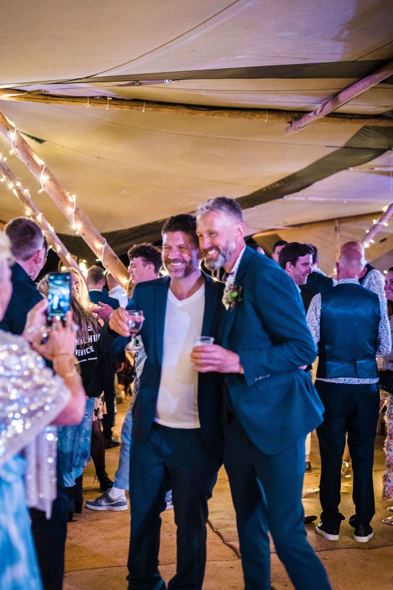 Wedding reception party under a tent with string lights and guests dancing on the dance floor.