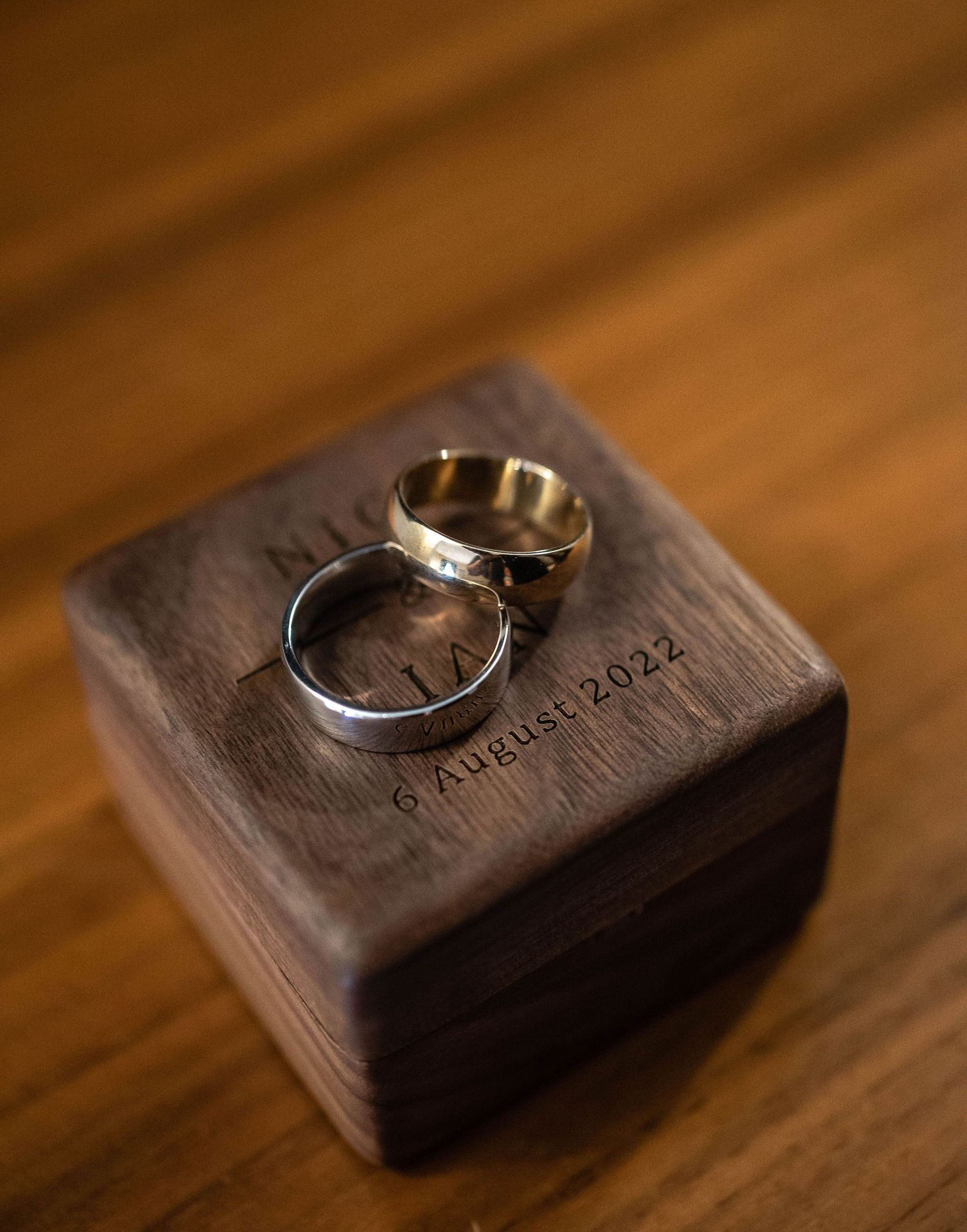 Two wedding bands resting on an engraved wooden ring box.