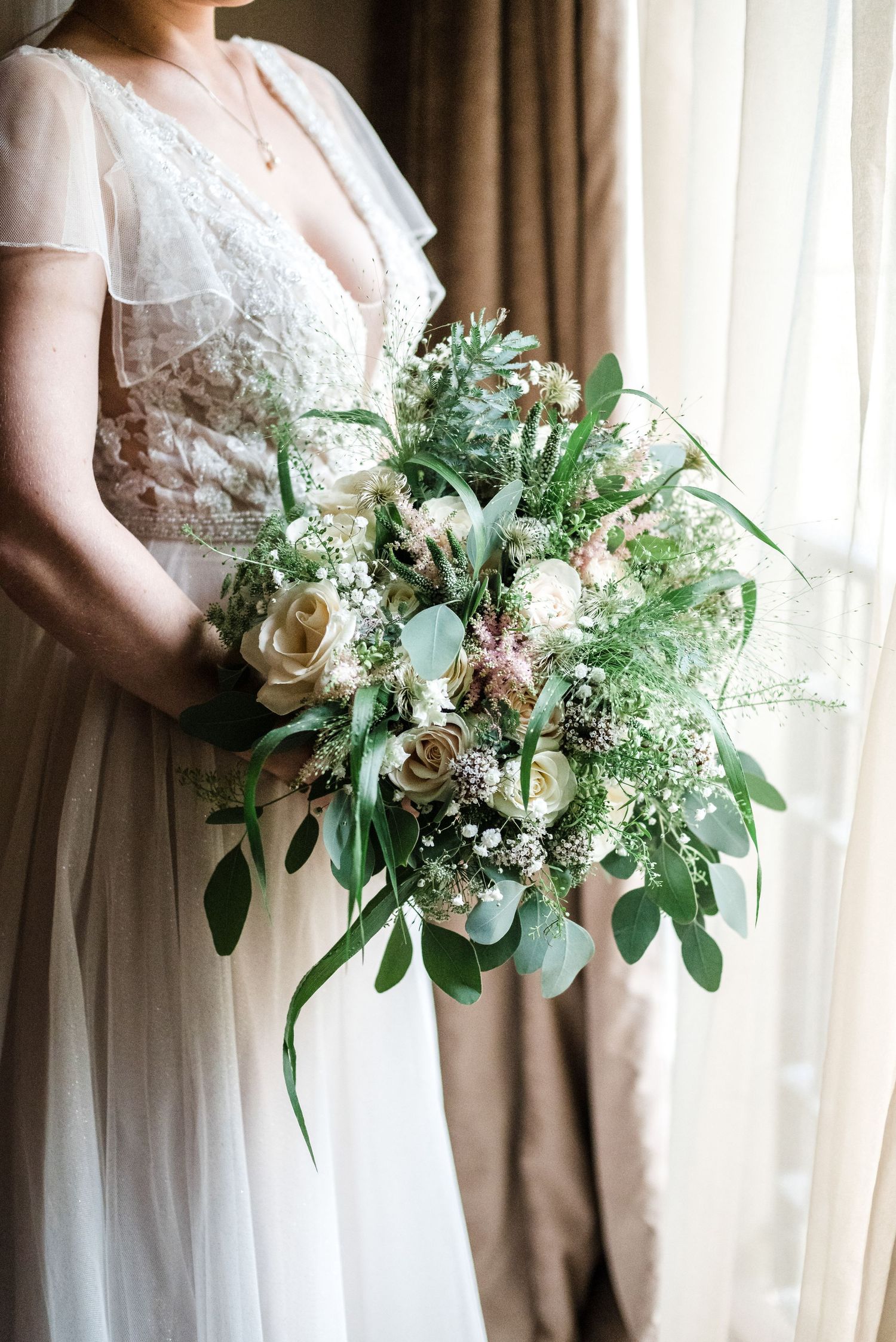 A wedding bouquet with white roses, greenery and delicate baby's breath against a white dress.