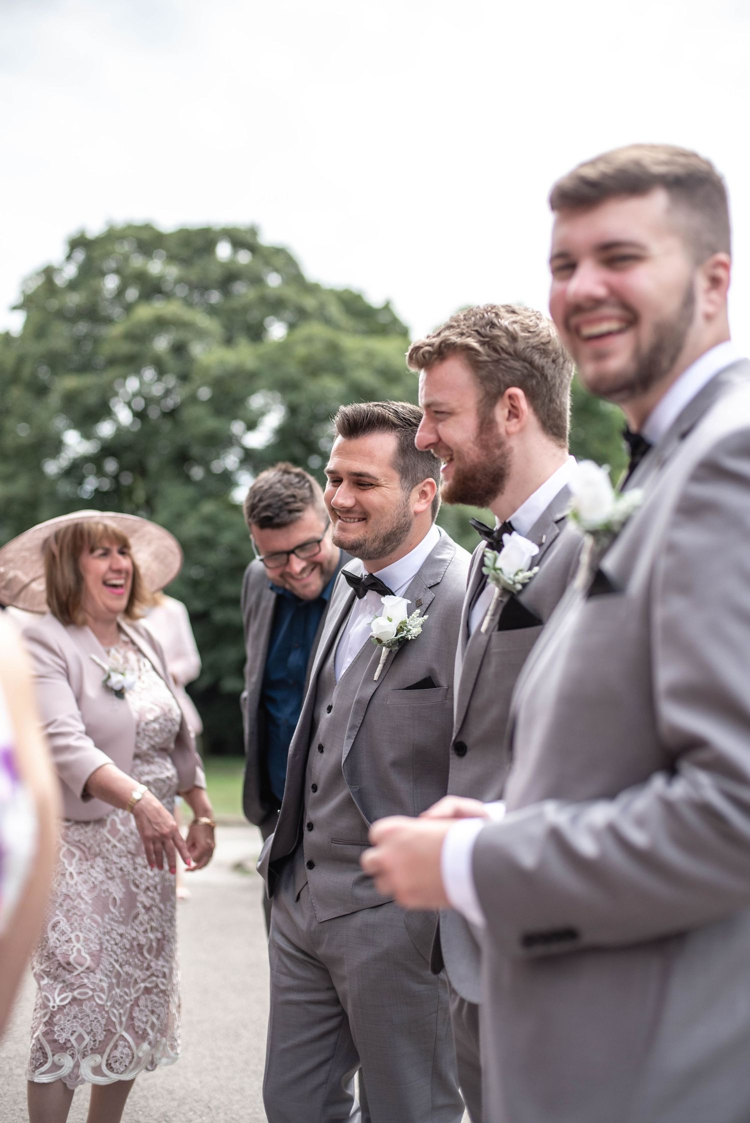 Wedding party sharing a candid moment outdoors in formal attire.