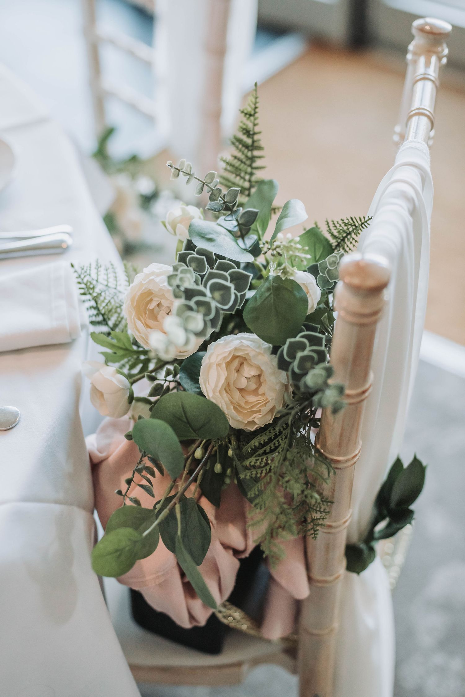Delicate floral arrangement with white roses and greenery rests on a vintage-style chair.