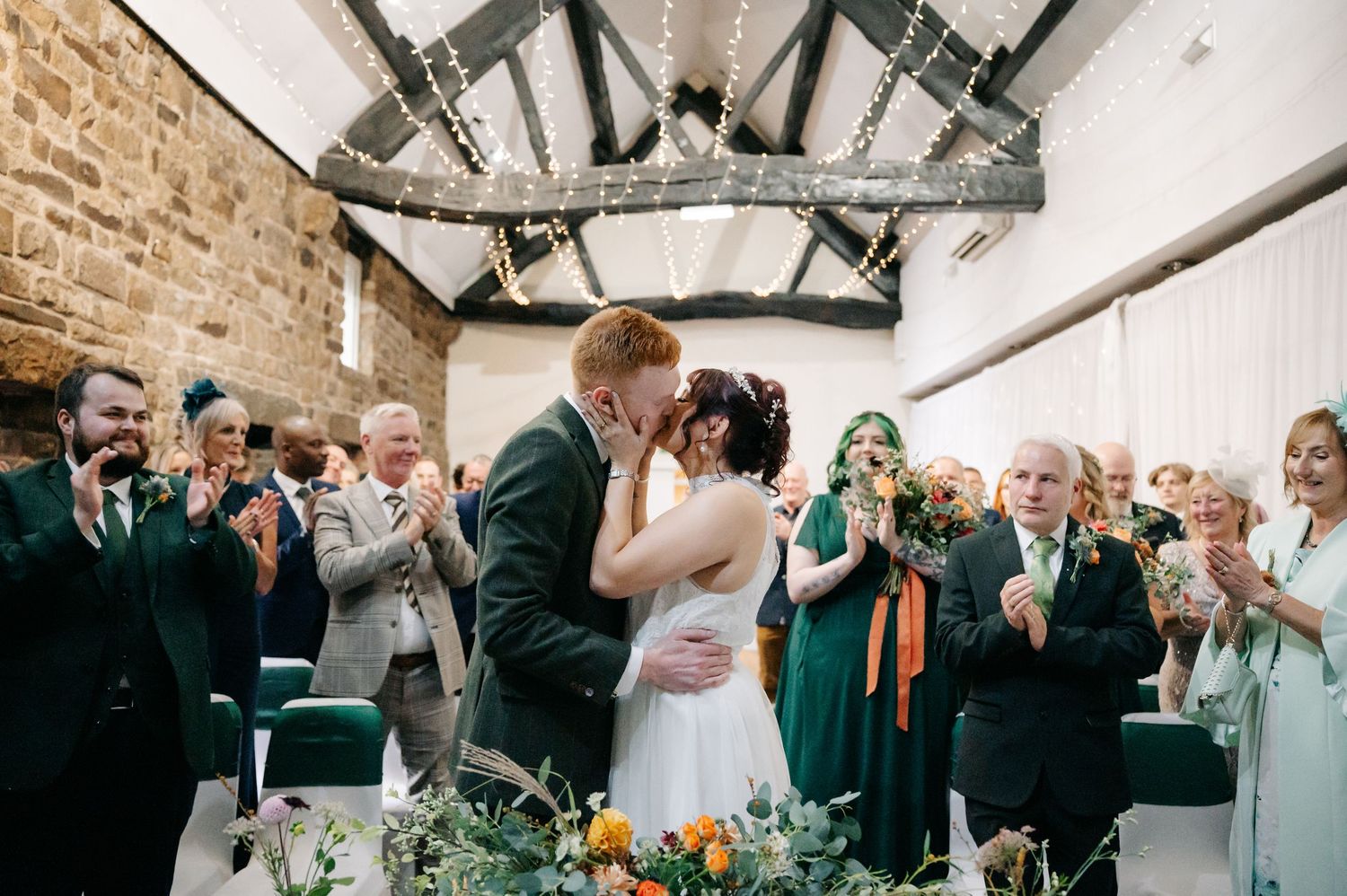 Wedding celebration in a rustic venue with exposed beams as guests applaud the newlyweds.