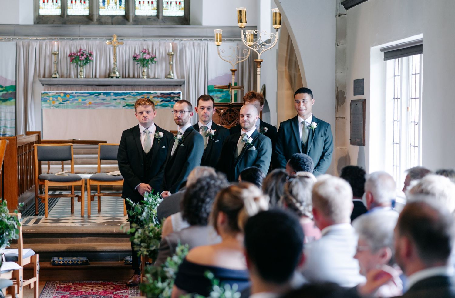 A panoramic view of a traditional church wedding ceremony with guests seated in wooden pews and greenery decorations.