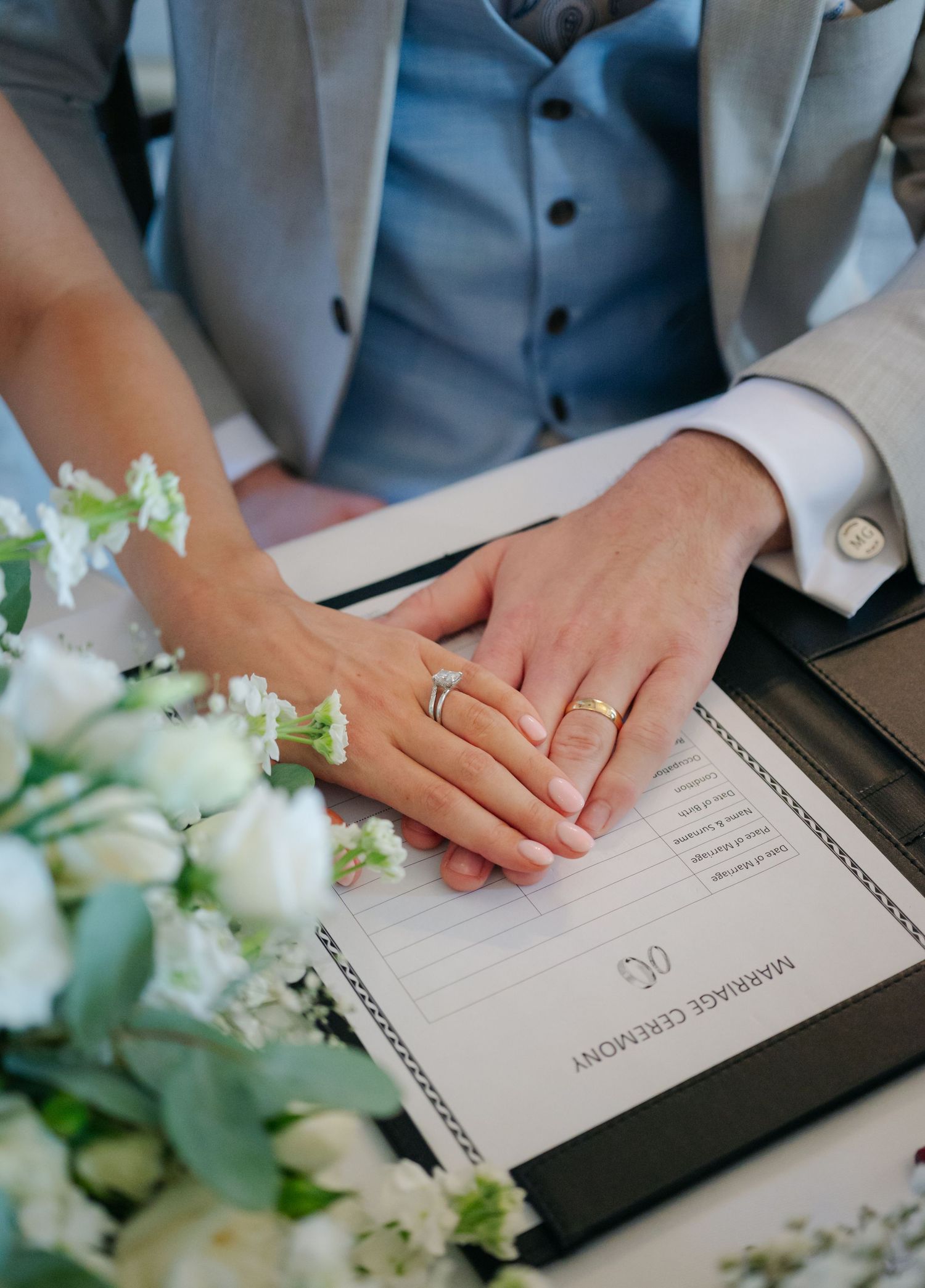 Wedding document signing with close-up of hands and white floral decorations on a dark surface.