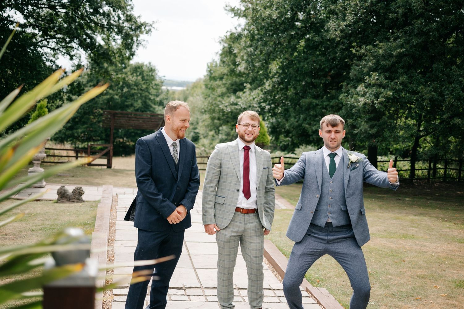 Groomsmen in gray suits walk together outdoors on a sunny day in a park setting.