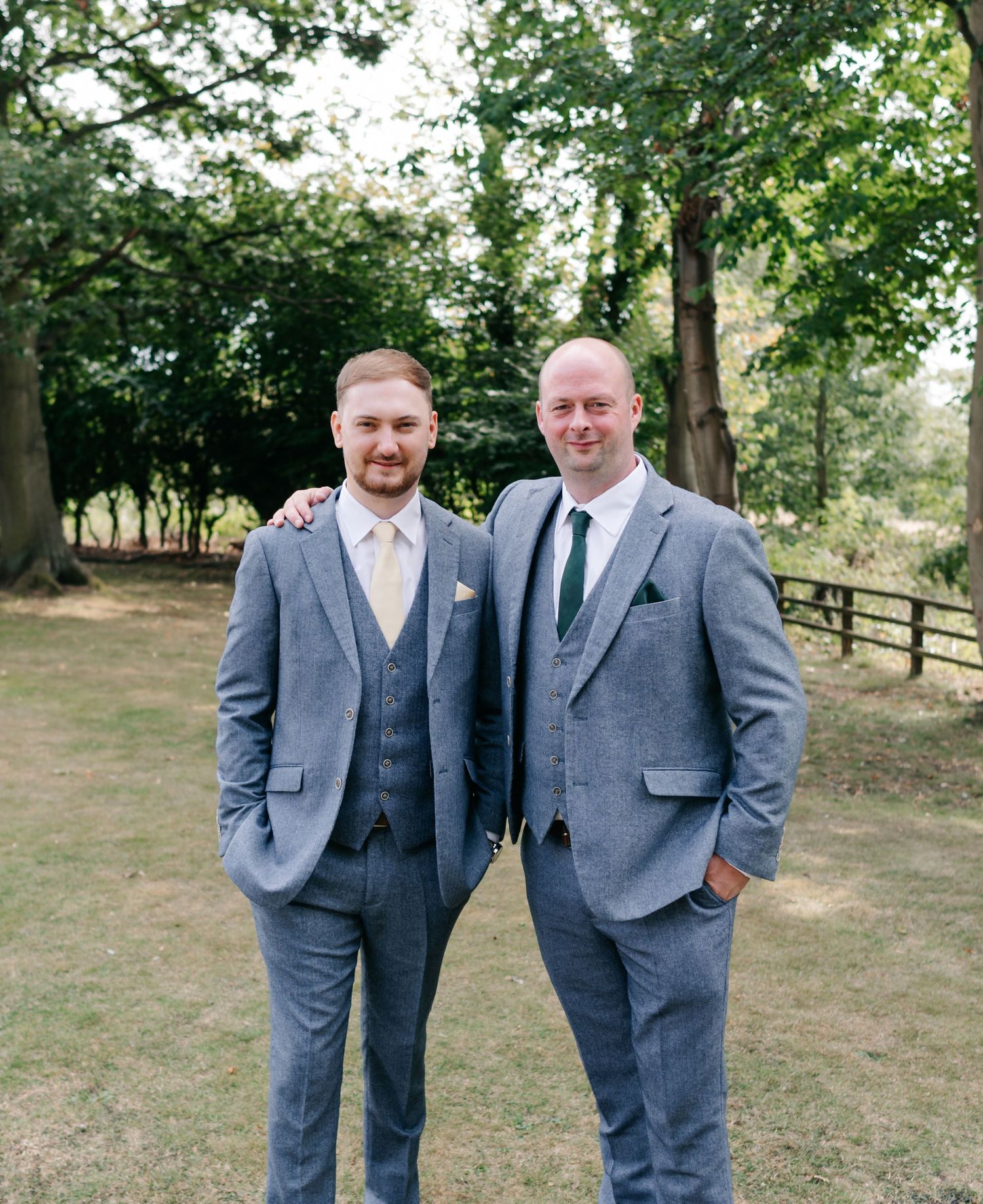 Groomsmen wearing matching gray suits with tan ties pose outdoors in a natural setting.