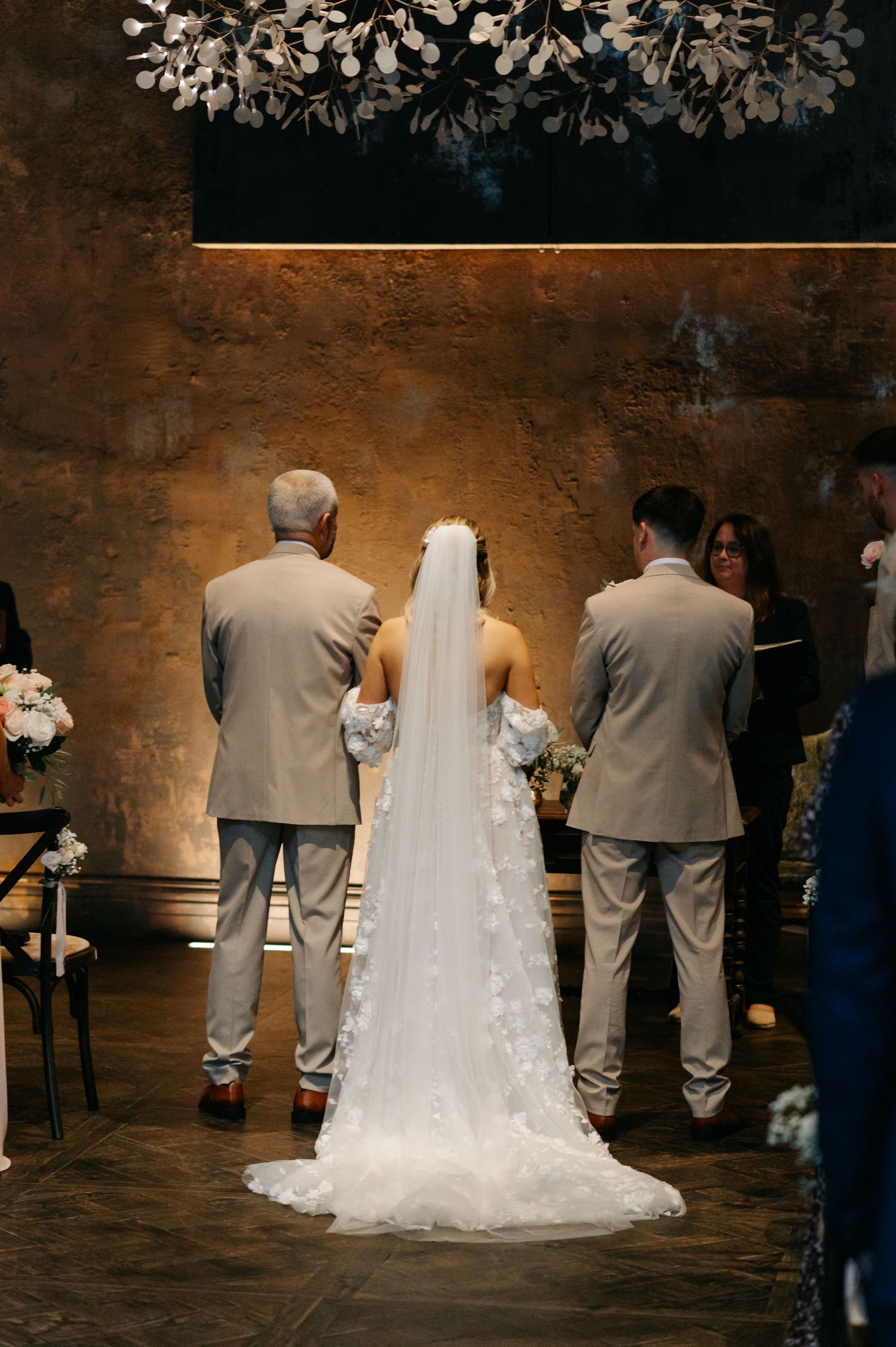 Wedding ceremony in a rustic venue with elegant floral decorations and guests in formal attire.