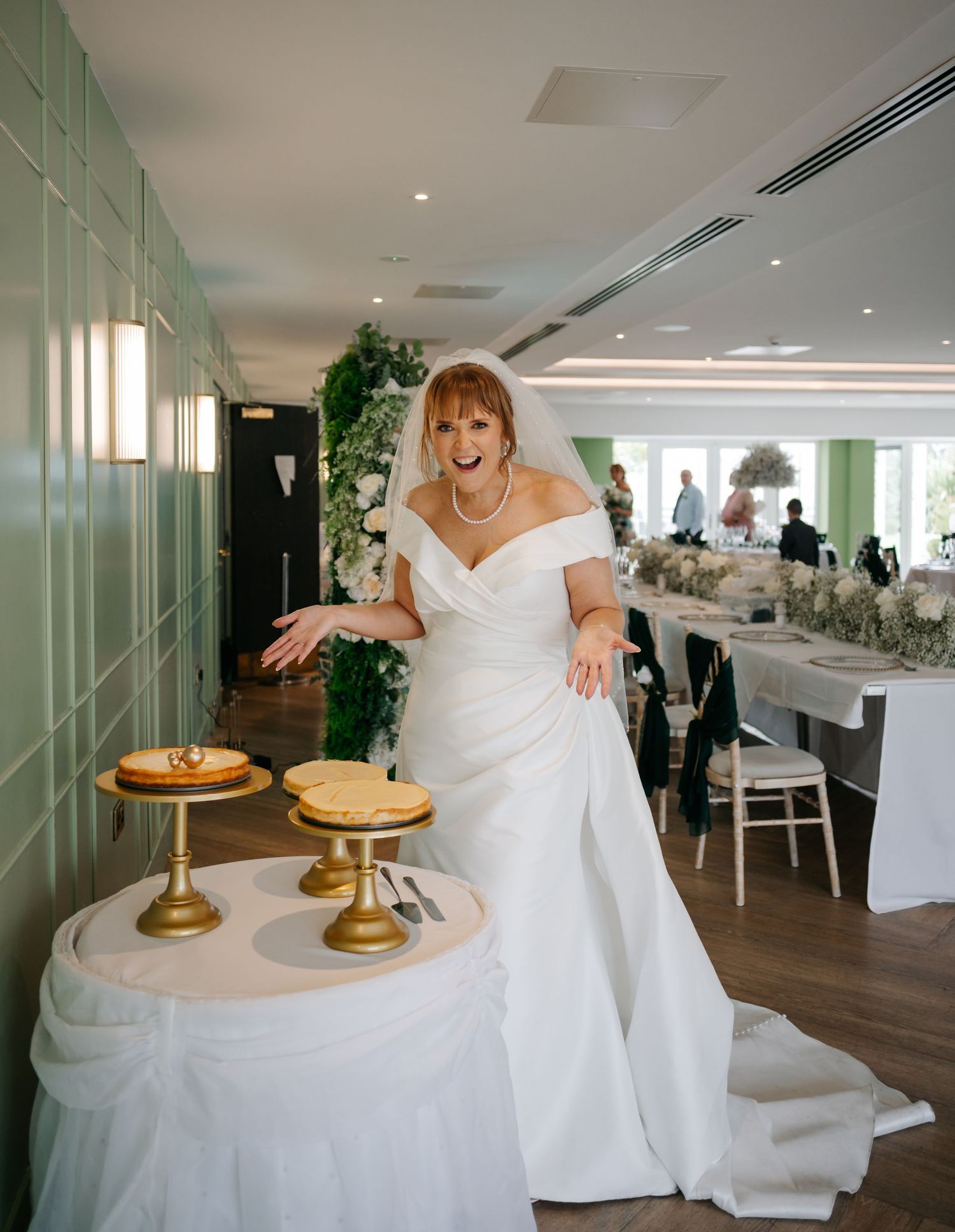 Modern wedding reception venue with white decor, gold cake stands, and elegant table settings.