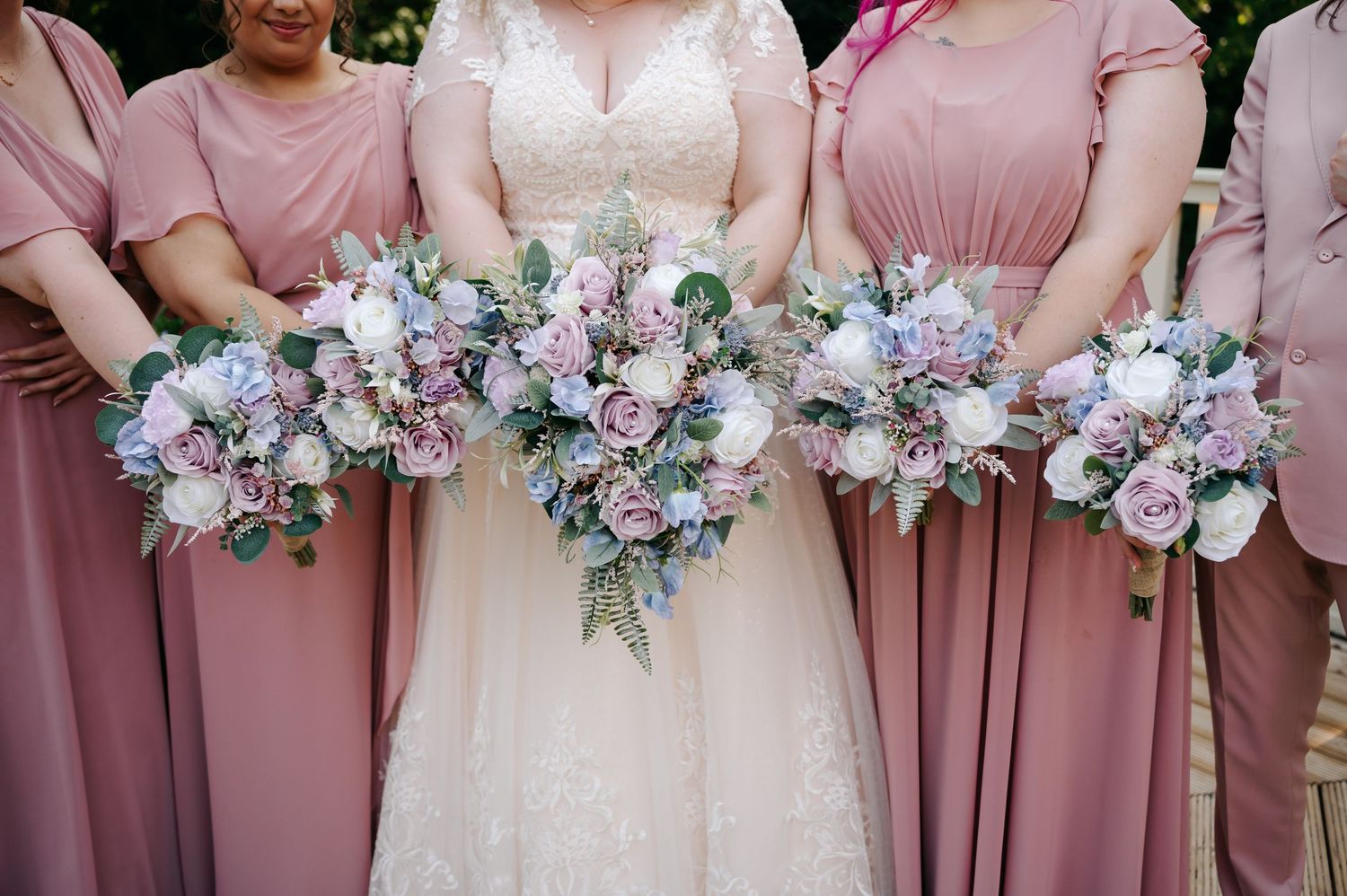 Bridesmaids in dusty rose gowns holding cascading pastel bouquets with bride in lace wedding dress.