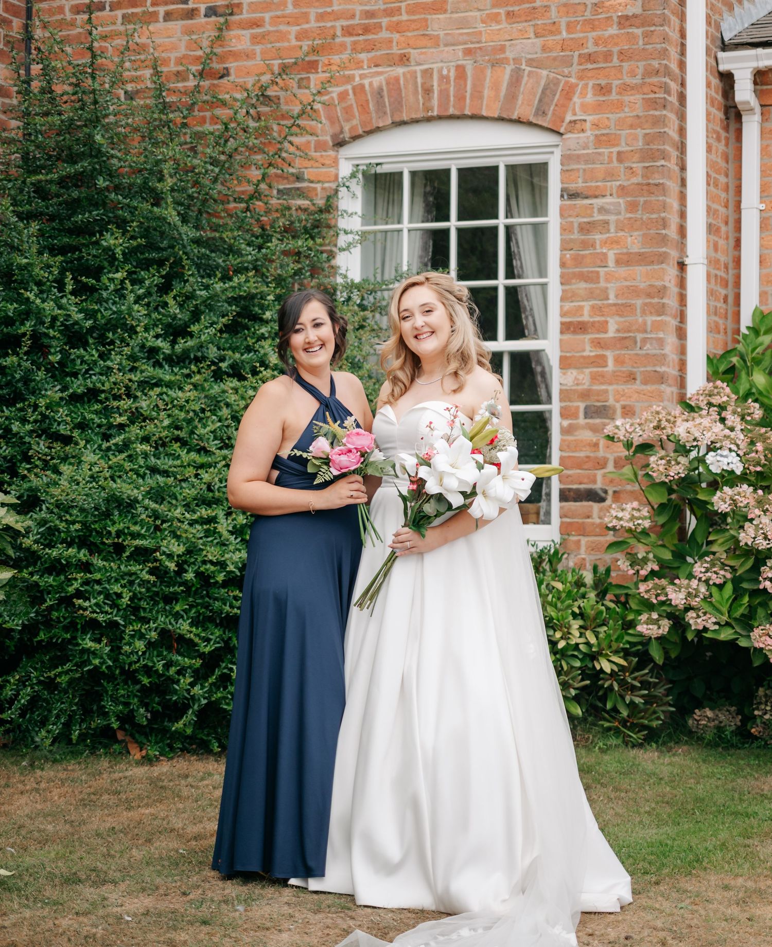 A wedding party poses for photos outside a classic brick building with blooming gardens.