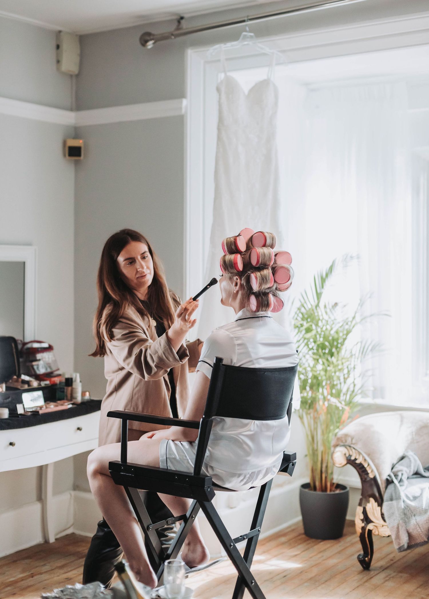 Behind the scenes of wedding preparation with makeup artist working in bright natural light.