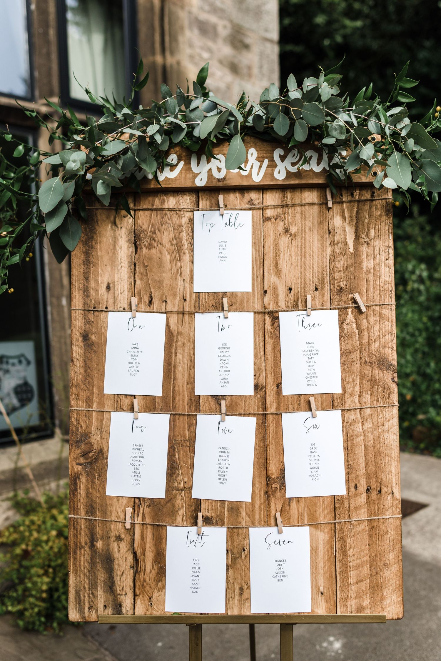 Rustic wooden seating chart display decorated with eucalyptus garland.