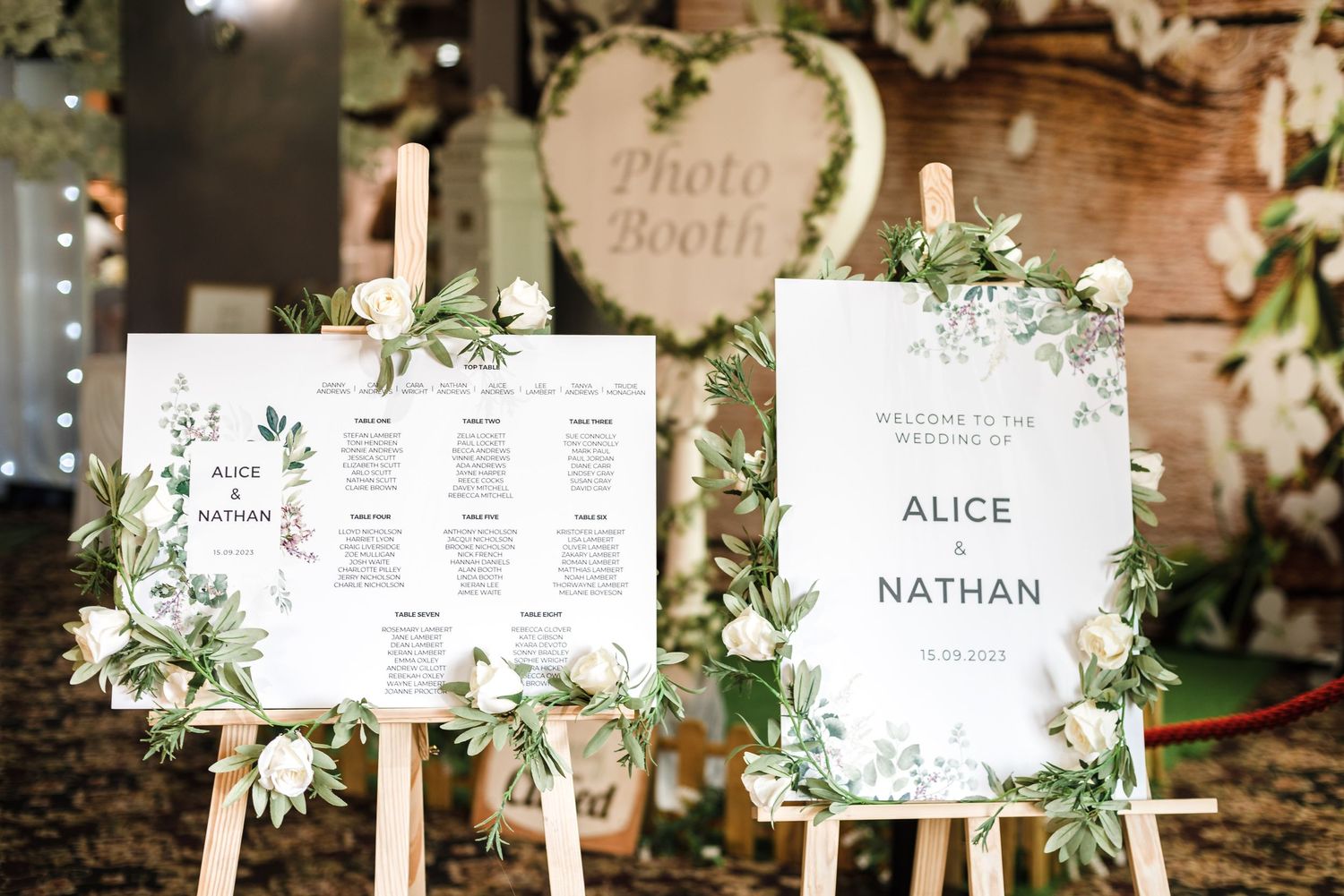 Elegant wedding seating chart displays with greenery decorations on wooden easels.