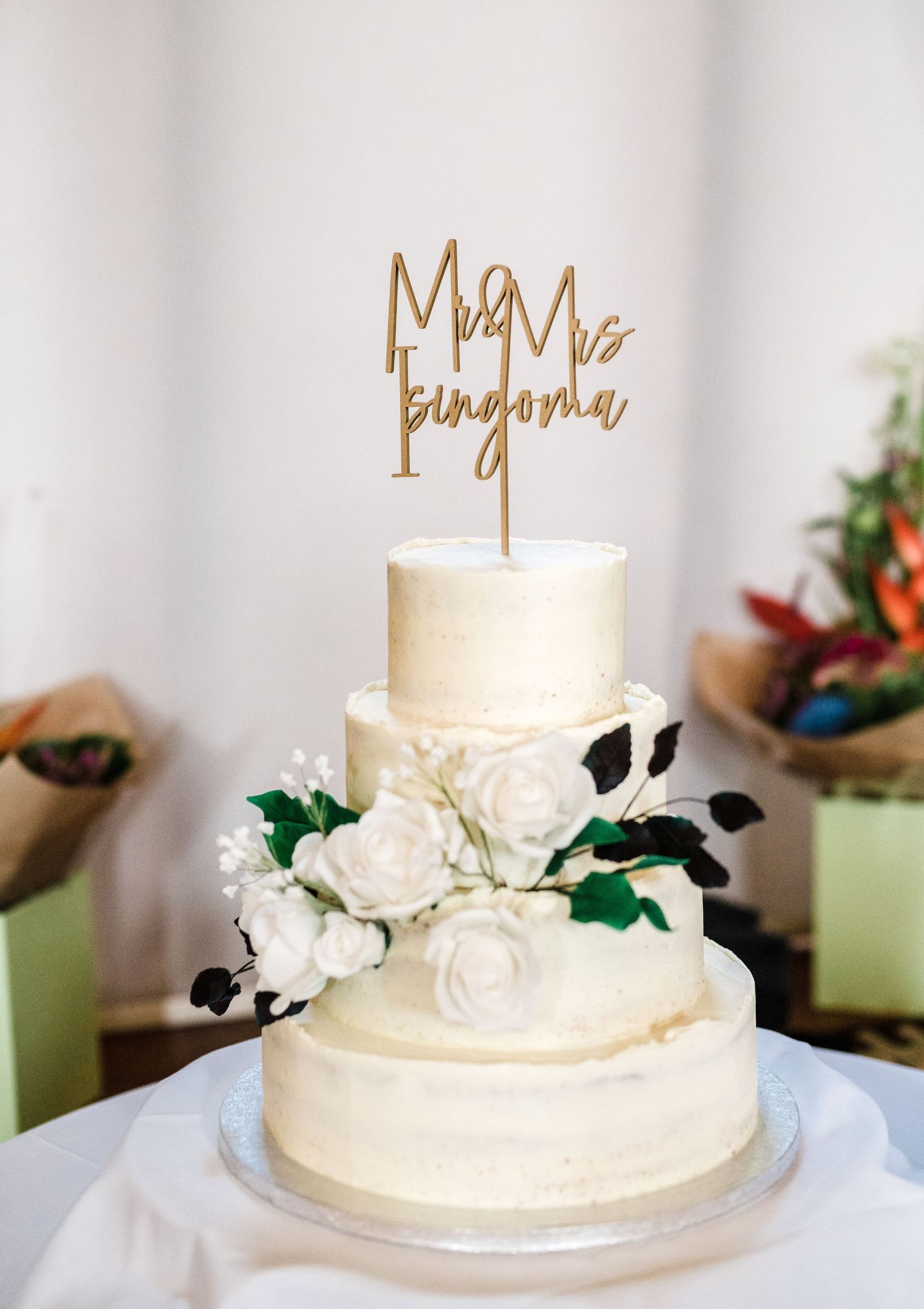 Three-tiered white wedding cake decorated with roses and gold 'Mr & Mrs' topper.