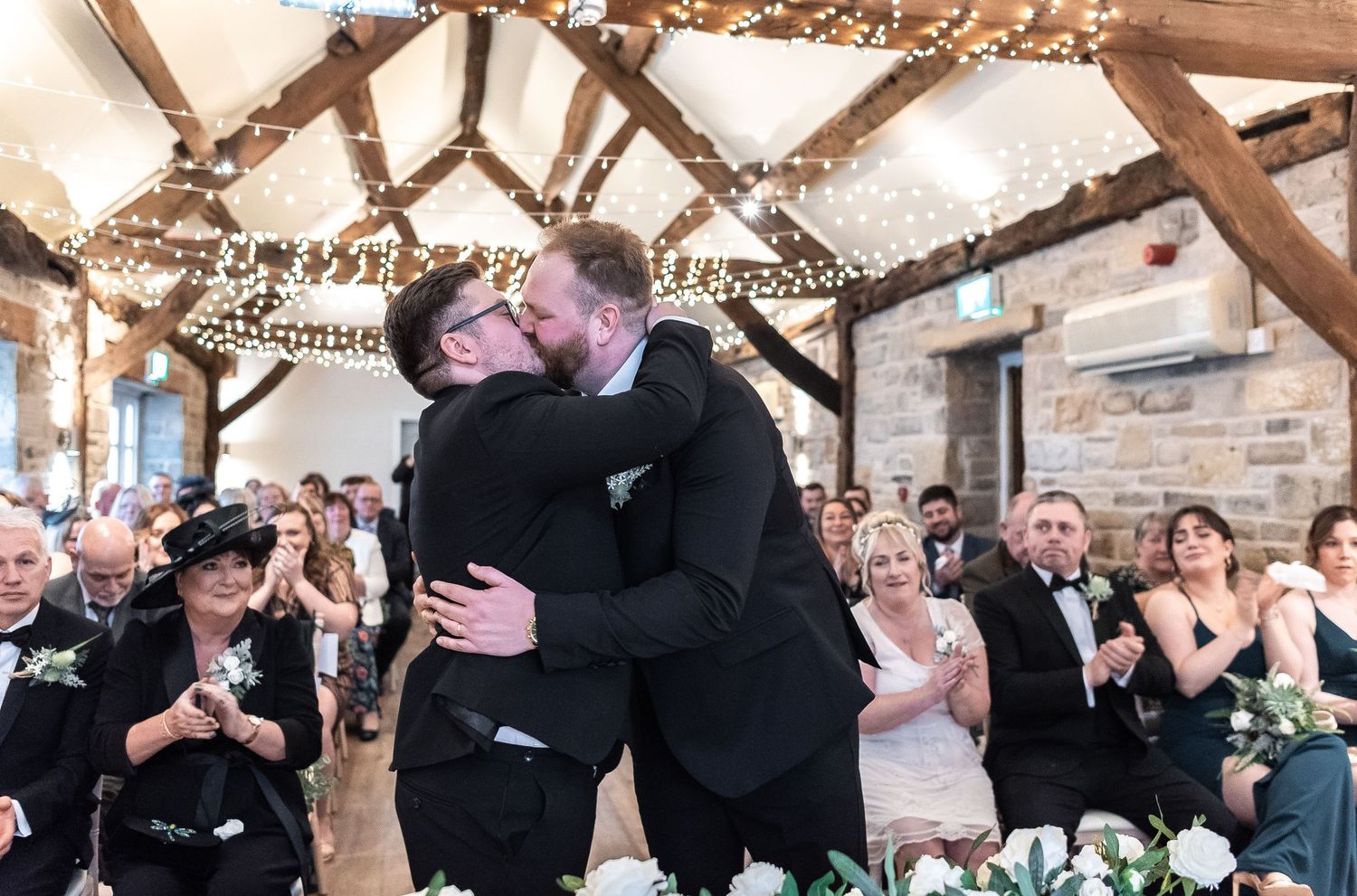 Celebratory moment during wedding ceremony under wooden beams with twinkle lights.