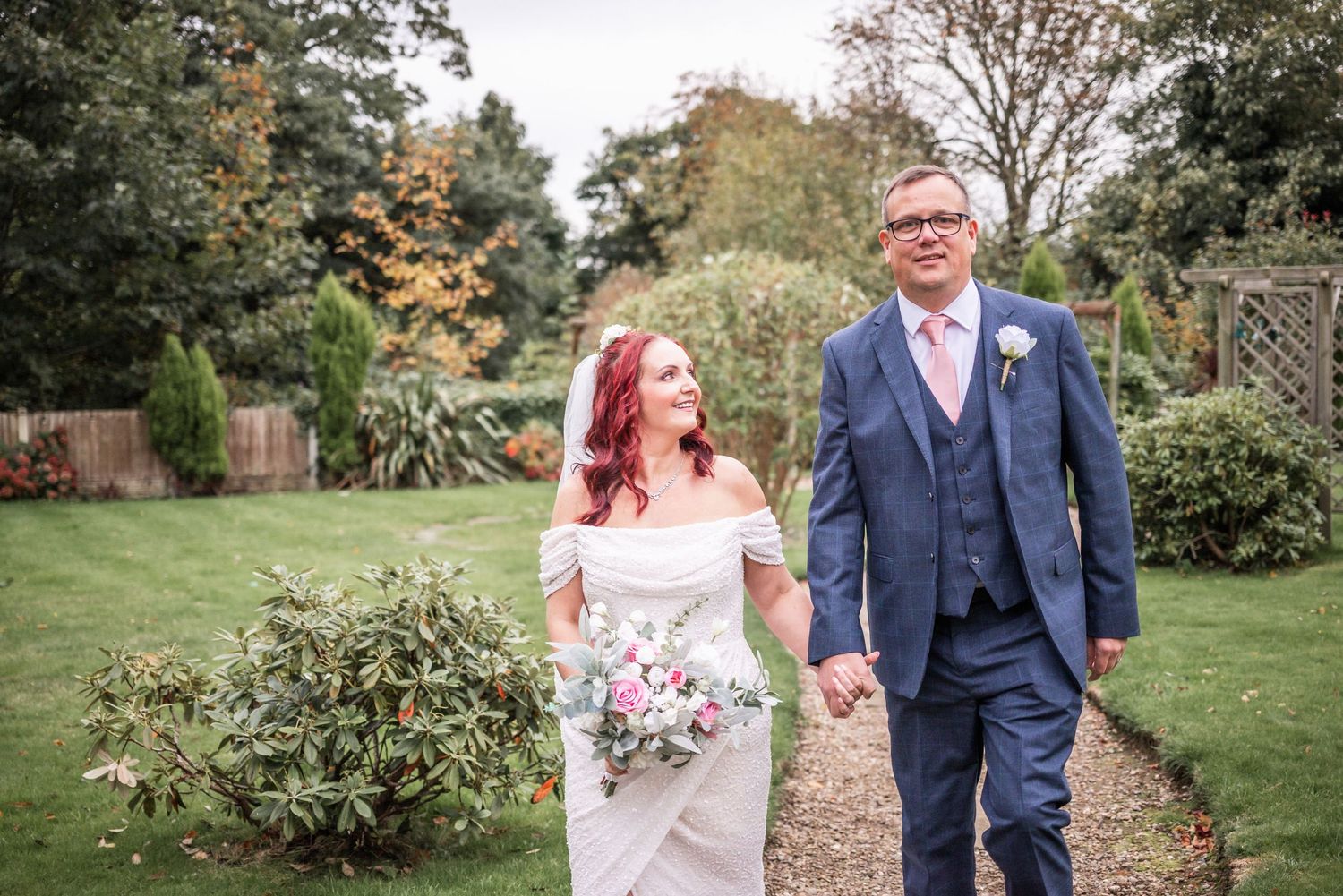 A couple walks together on a garden path during their autumn wedding celebration.