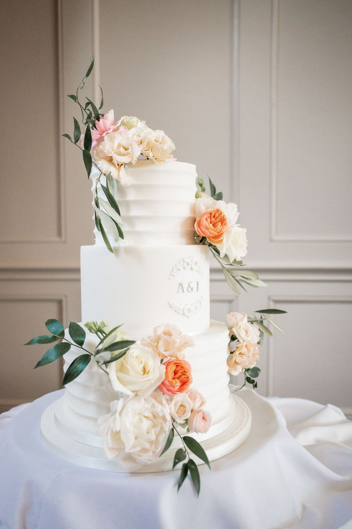 White tiered wedding cake decorated with peach and cream roses and eucalyptus leaves.