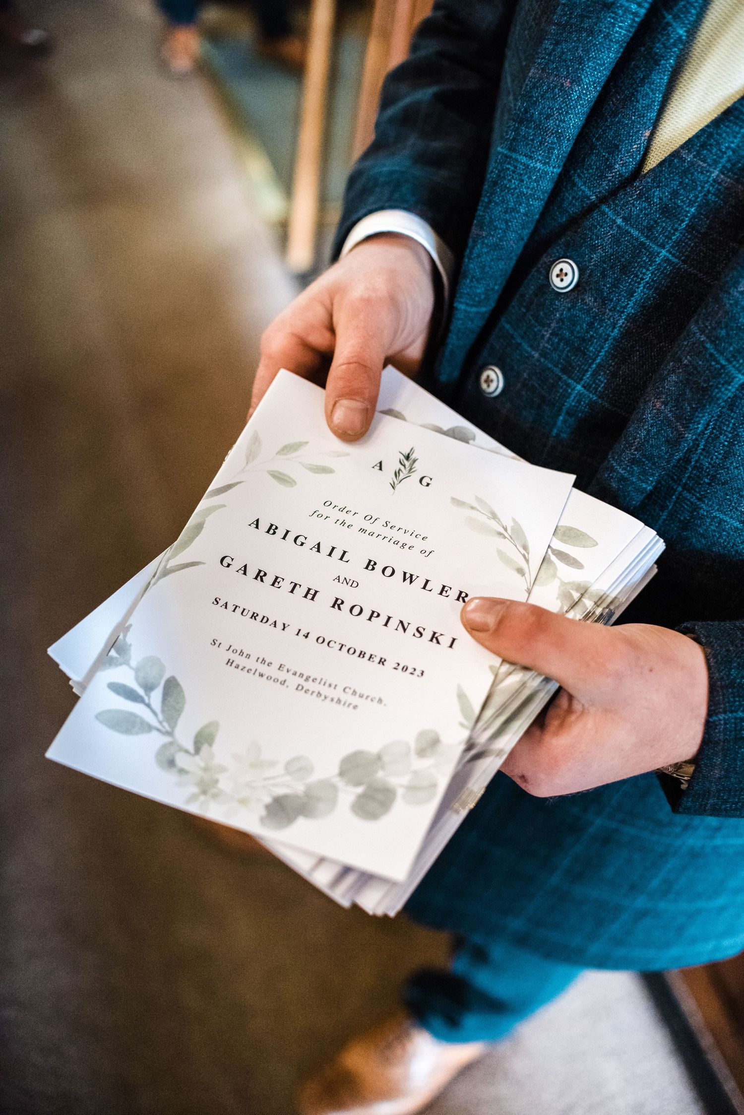 Wedding invitation with elegant floral design and minimalist typography held in blue suited hands.