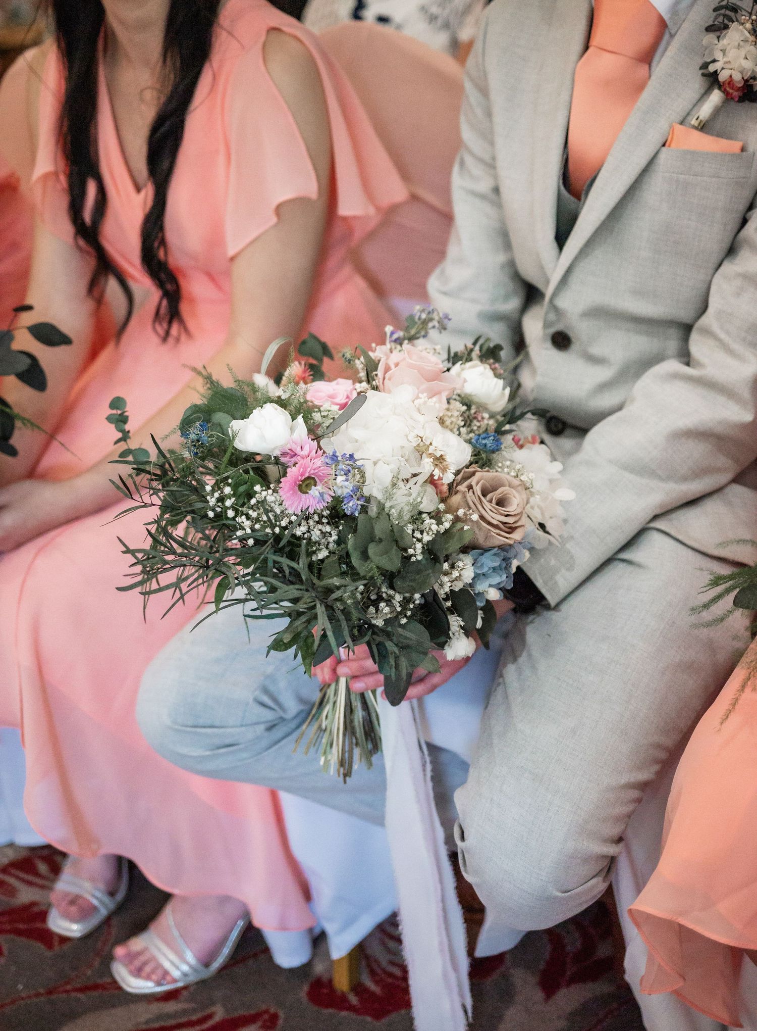Beautiful wedding bouquet with mixed flowers rests on coral and grey attire.