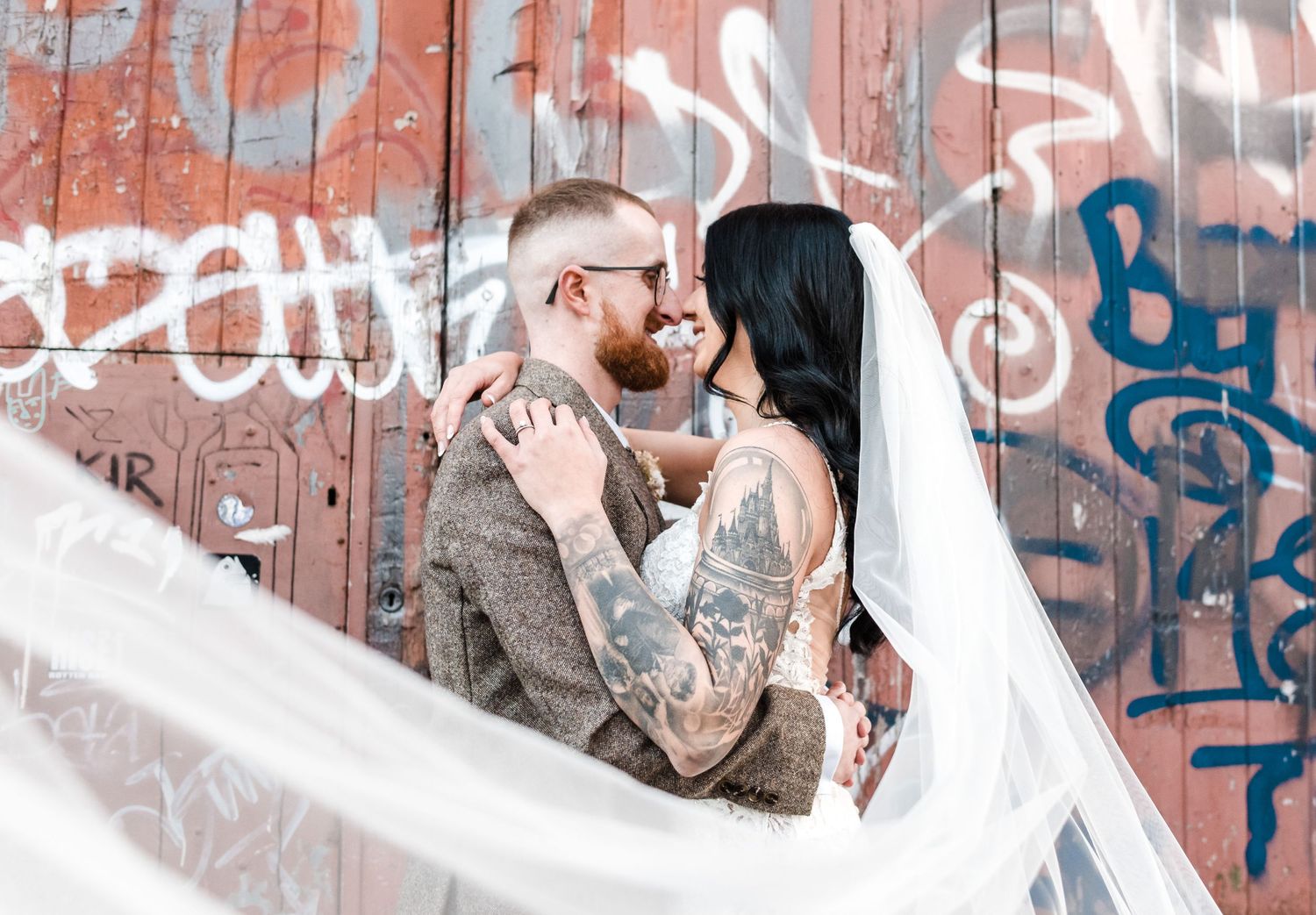 Wedding couple embraces in front of graffiti covered wall with flowing veil.