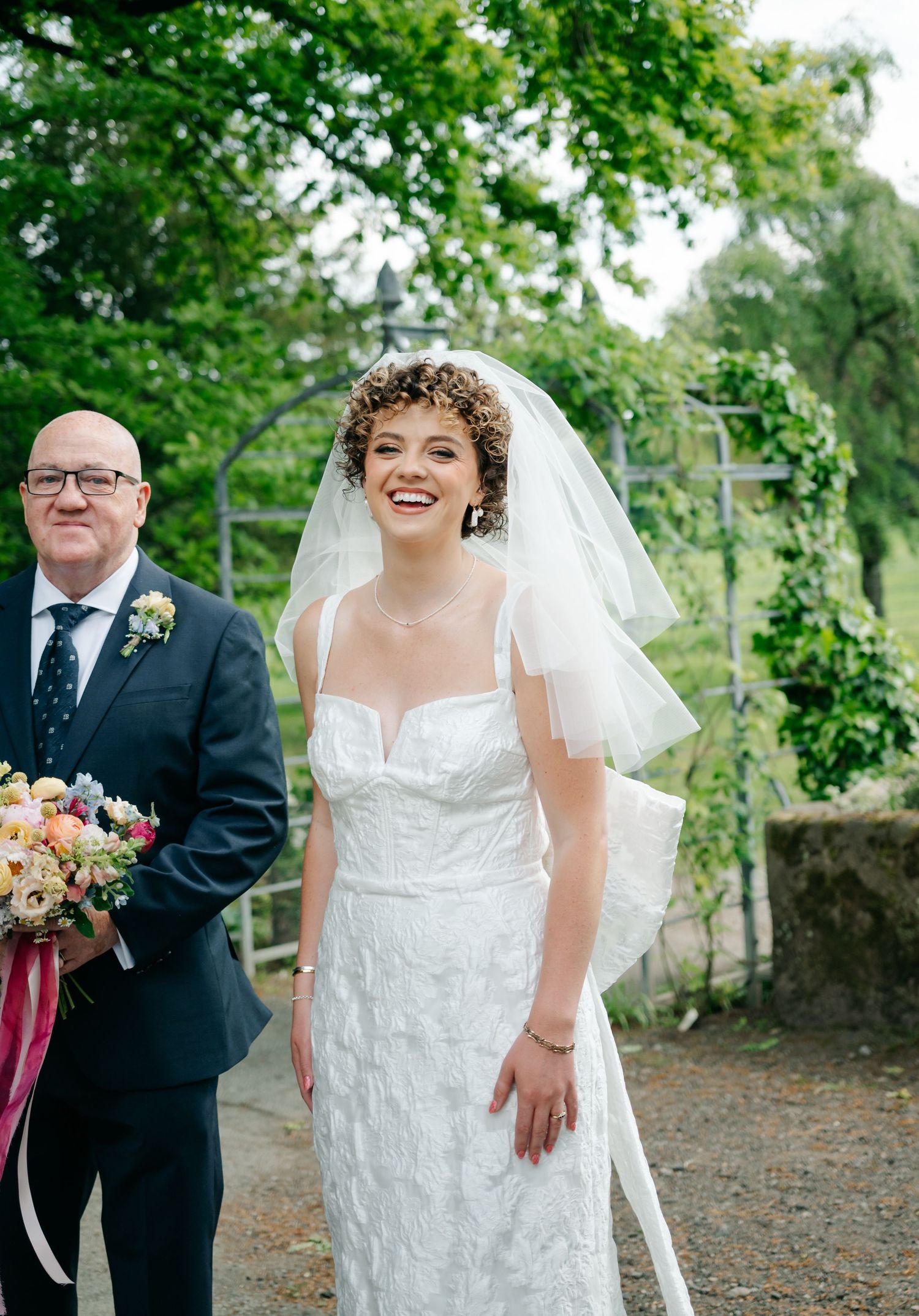 A beautiful wedding scene outdoors with lush greenery and white decorations.