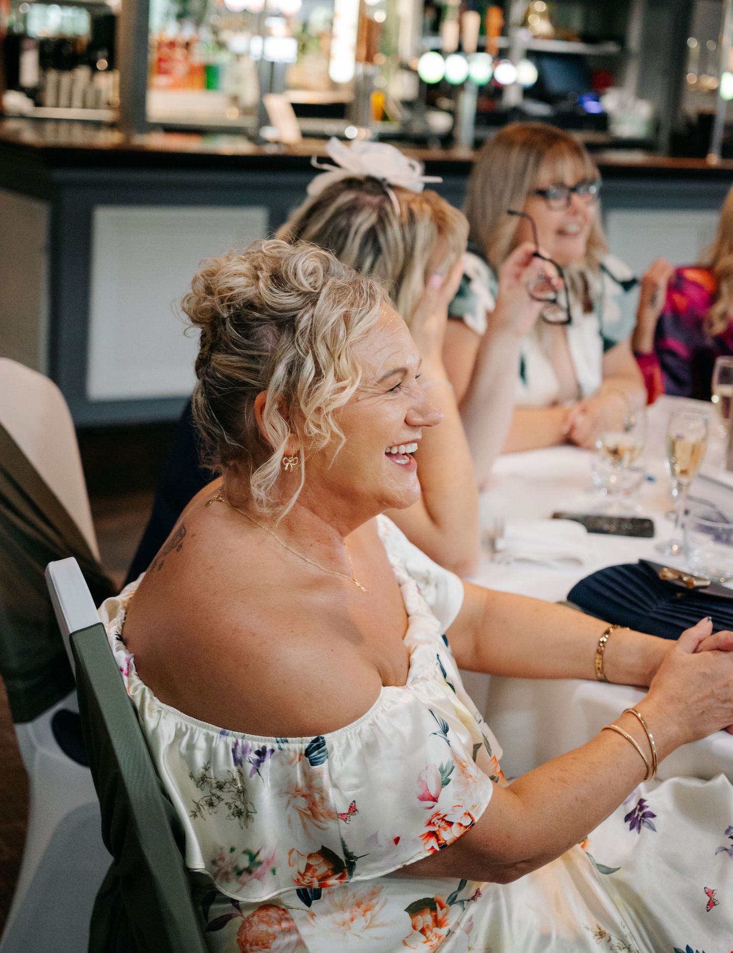 A guest in a floral dress laughs during a wedding reception.