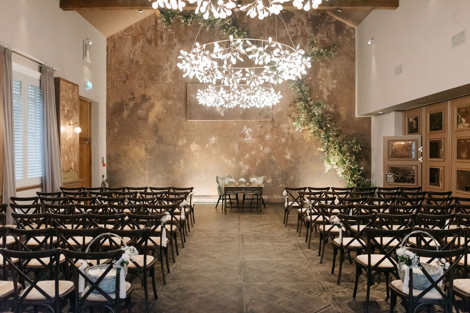 Elegant wedding venue setup with rows of white chairs and sparkling chandeliers in a rustic industrial space.
