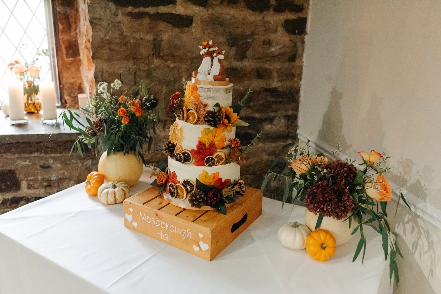 Rustic fall table setting with orange pumpkins and floral centerpieces against stone wall backdrop.