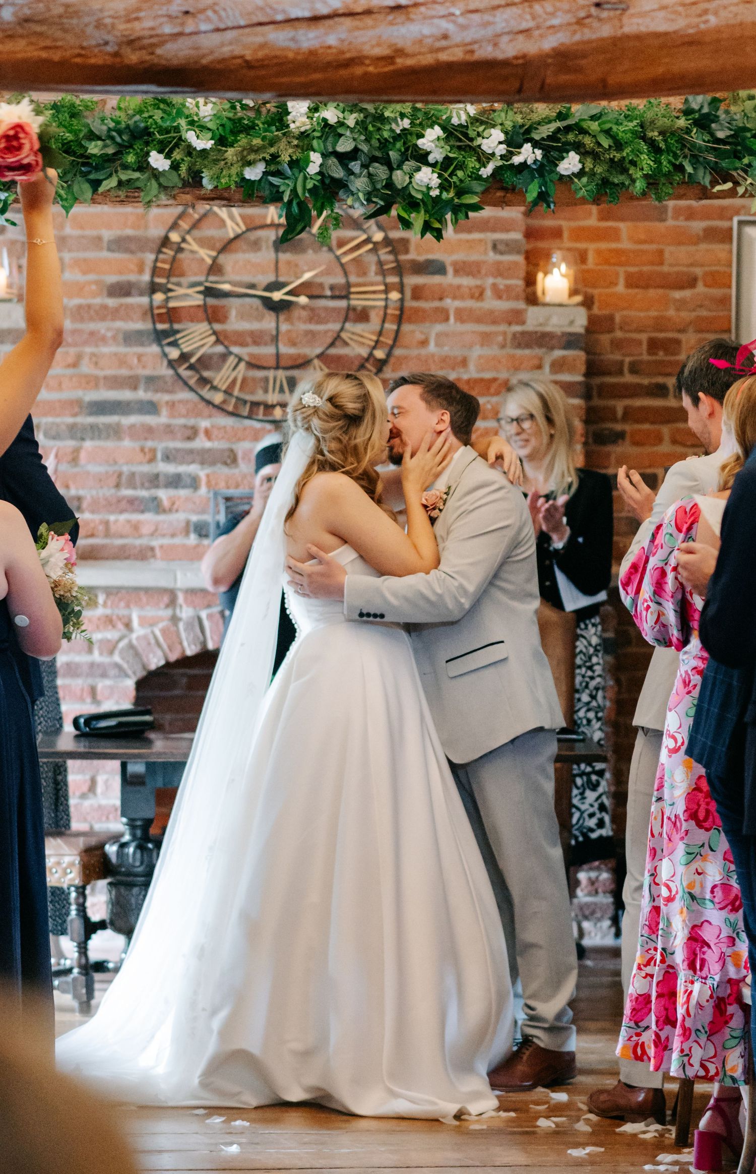 Newlyweds and guests dance in a beautiful rustic venue with exposed brick walls and hanging greenery.