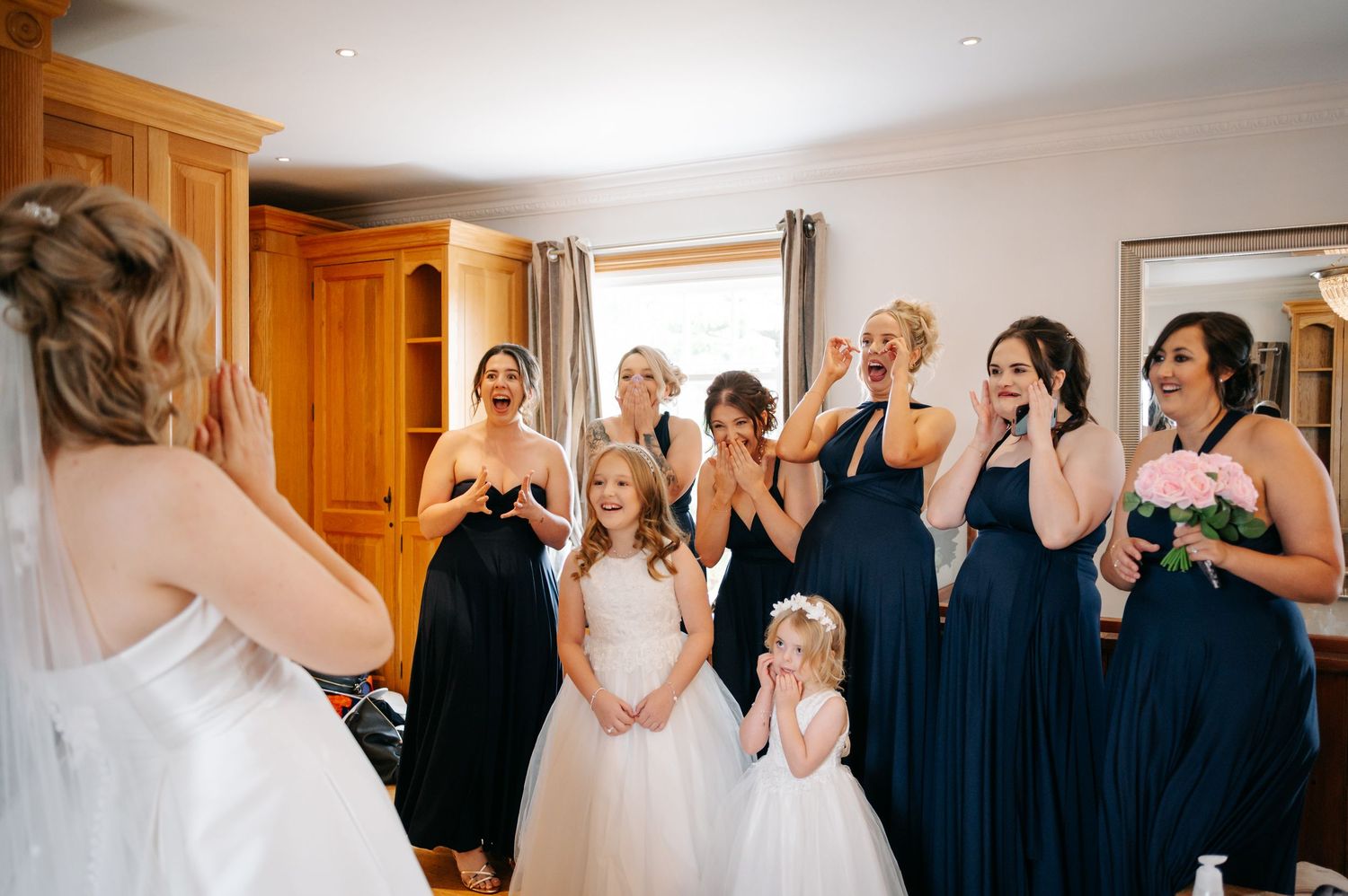 Wedding party getting ready together in a bright room with wooden cabinets and joyful expressions.